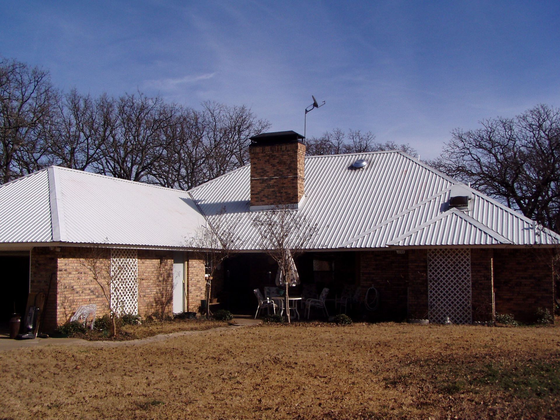 Brick house with a white roof and chimney, fronted by a large brown lawn and leafless trees.