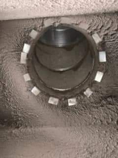 Close-up of a round metal pipe opening set in rough gray concrete with white spacers around the rim