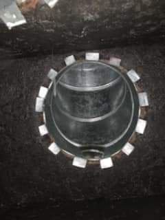 Black circular vent or pipe fitting with a silver ring and white tabs on a dark surface