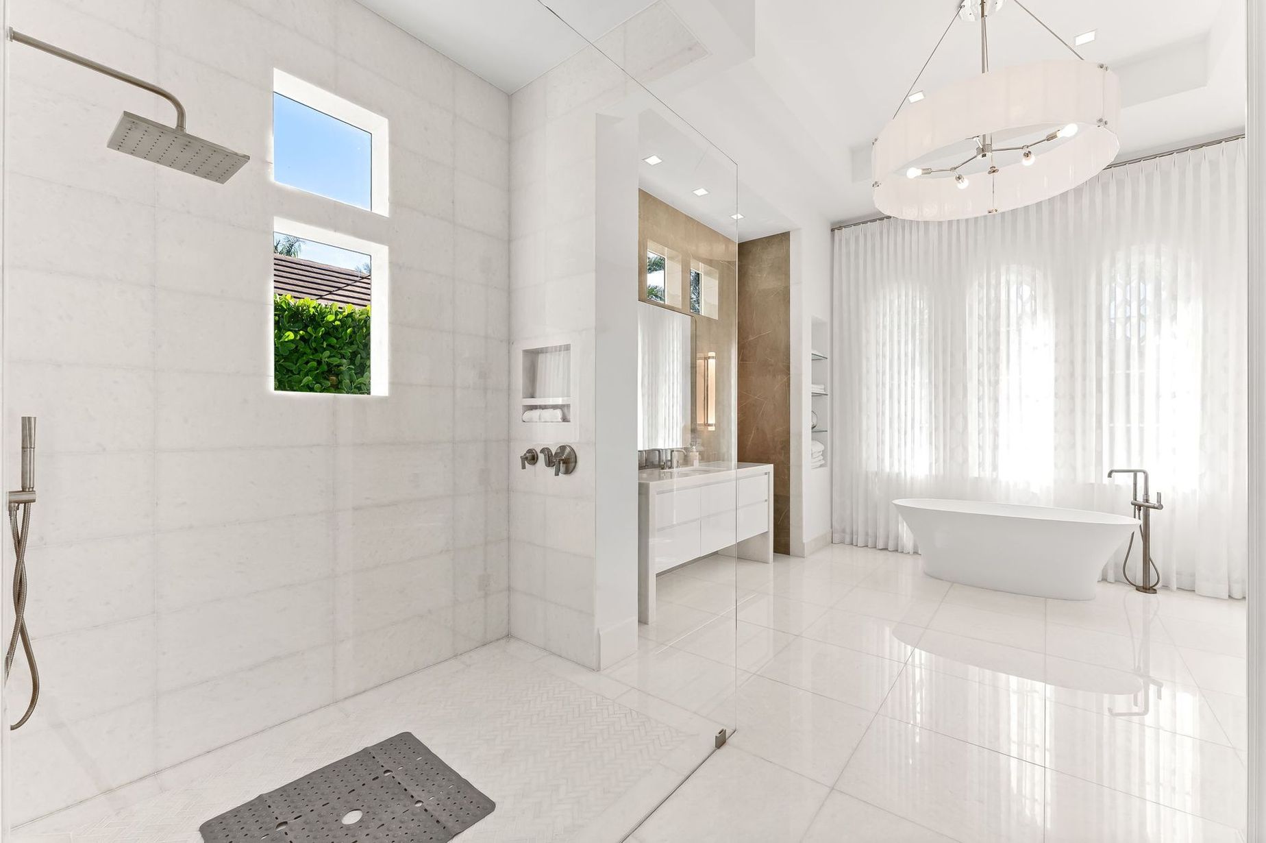 Bright white luxury bathroom with walk-in shower, freestanding tub, and large window with sheer curtains