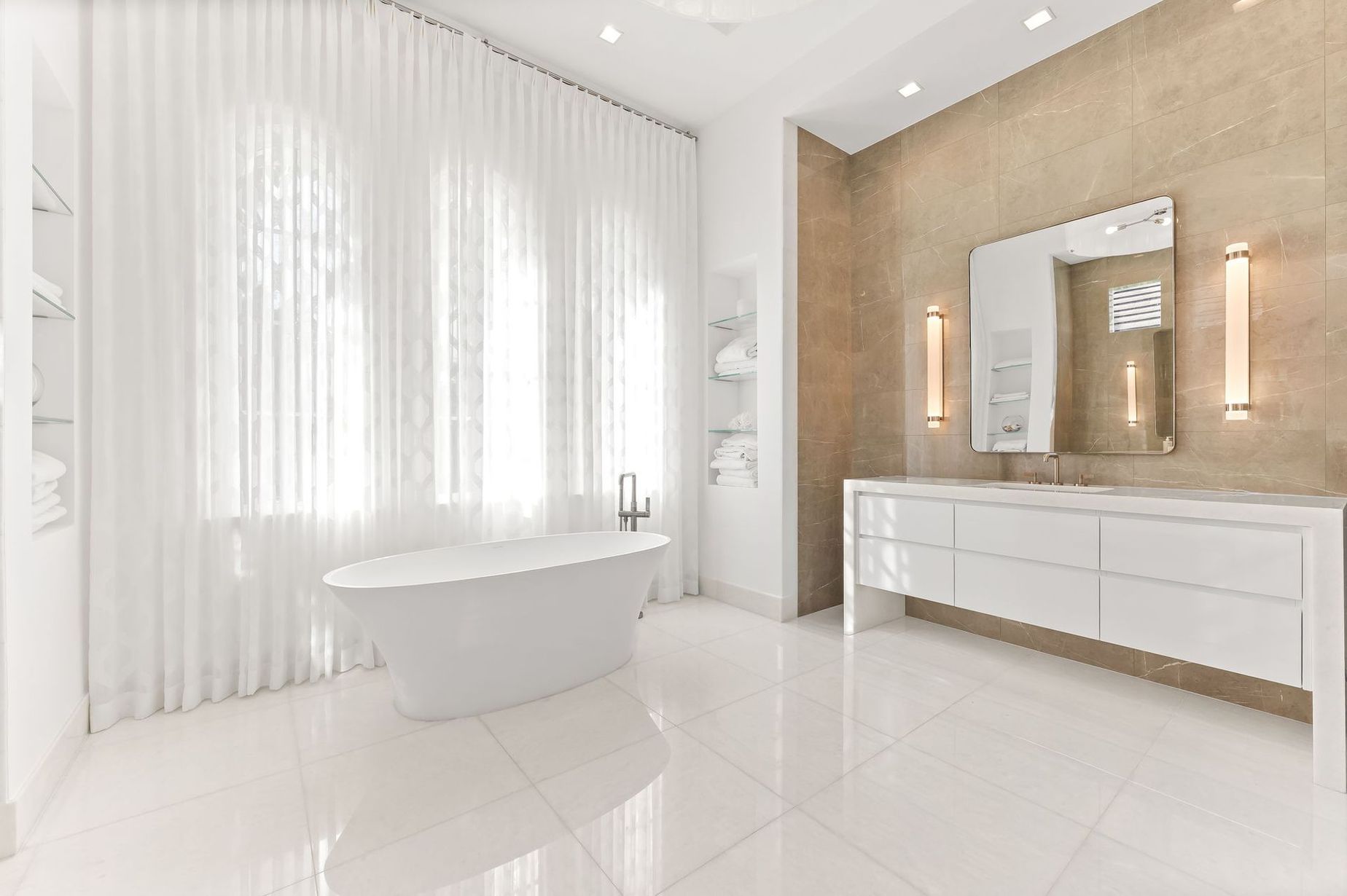 Bright white modern bathroom with freestanding tub, vanity, and sheer curtains.