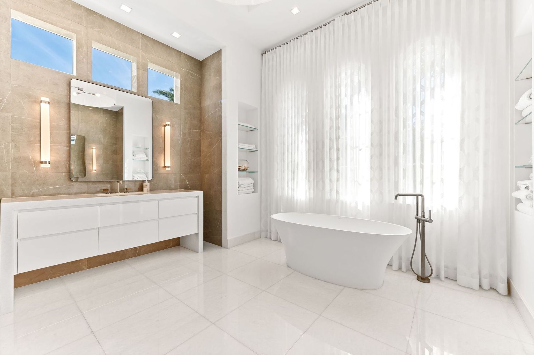 Bright modern bathroom with white vanity, freestanding tub, and sheer curtains over a large window