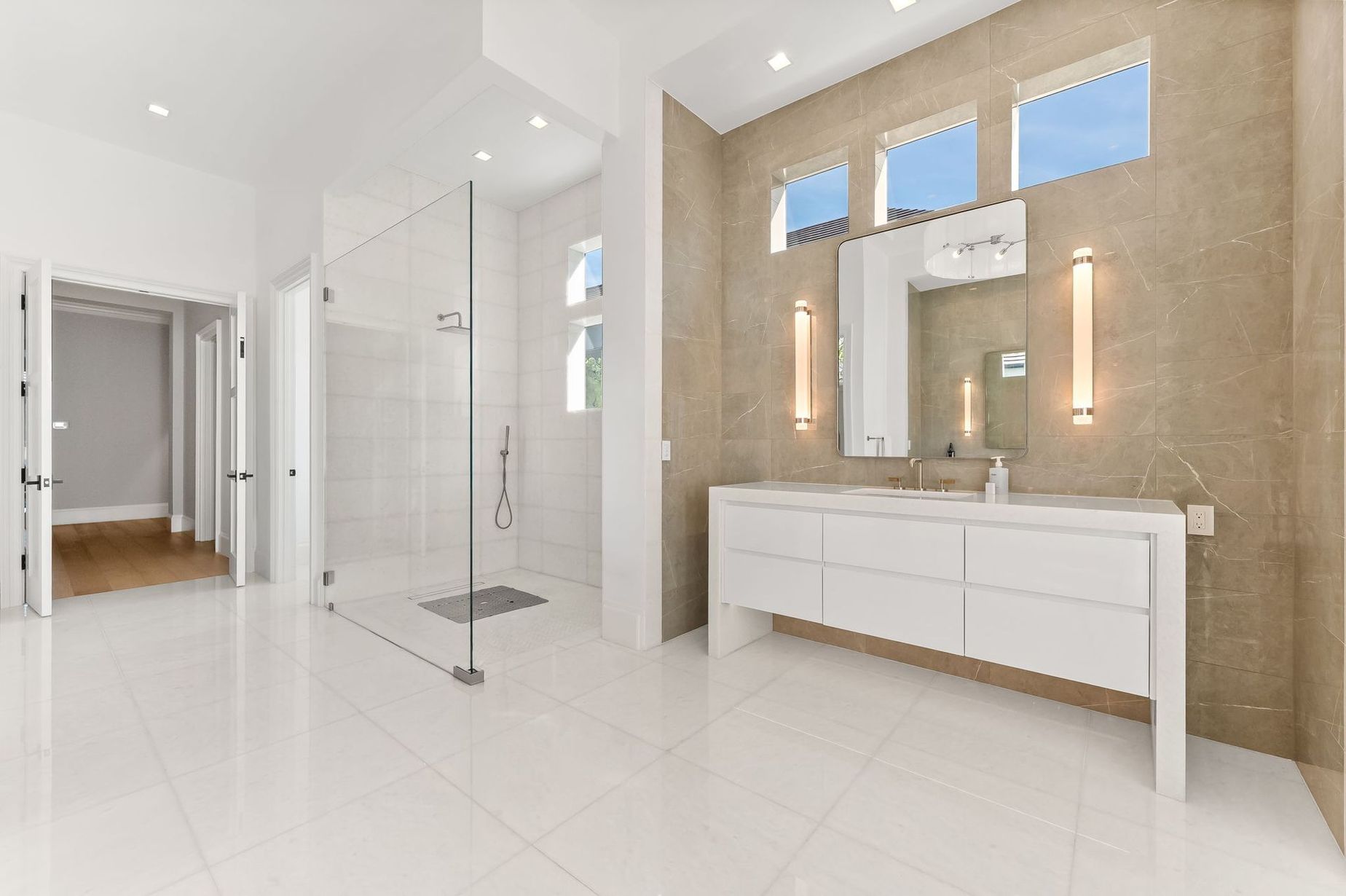 Bright modern bathroom with white tile, double vanity, large mirror, and glass shower.