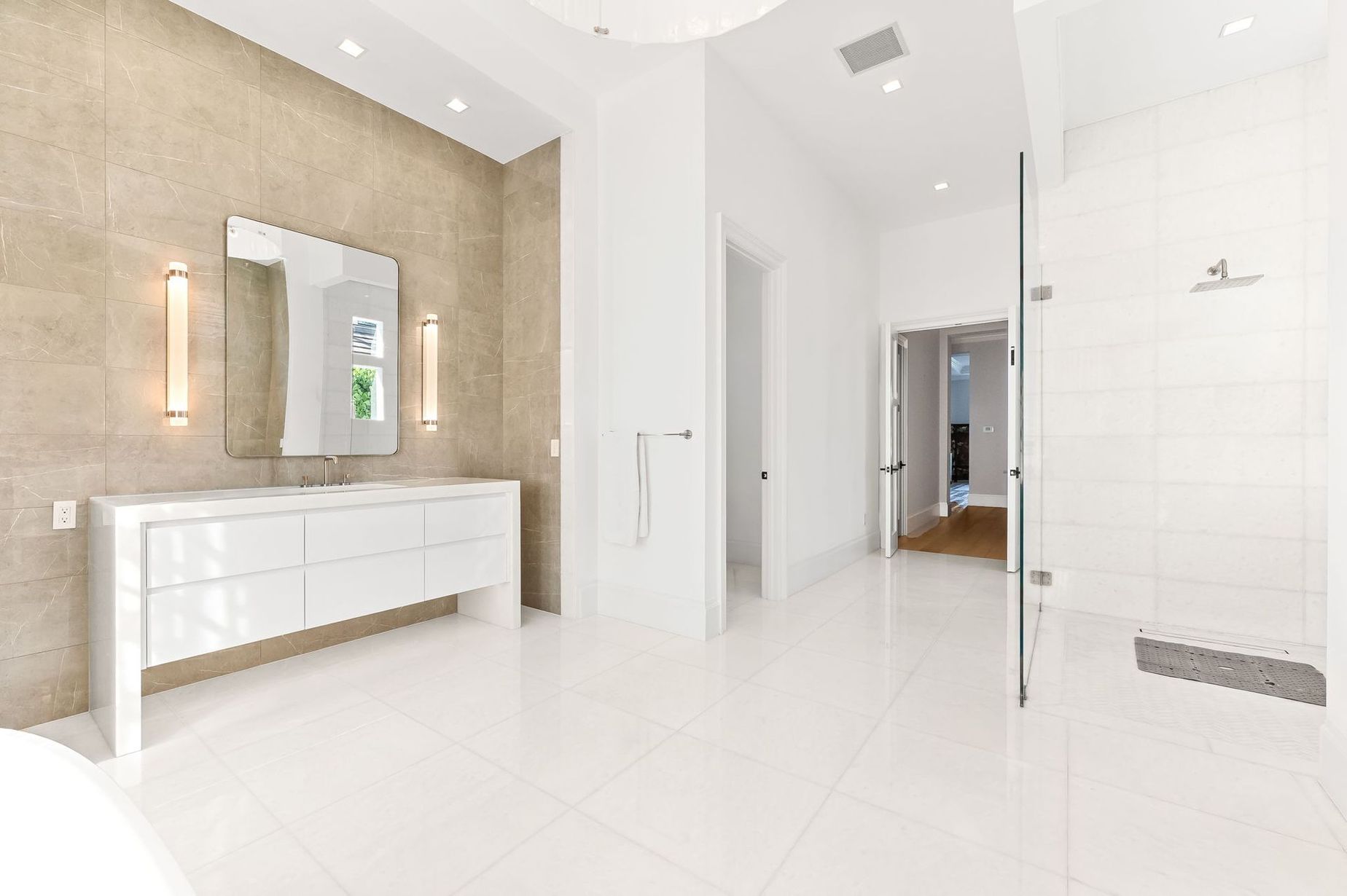 Modern white bathroom with double vanity, beige accent wall, glass shower, and bright tile flooring