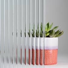 A succulent in a white and orange textured pot is visible through vertically ribbed, translucent glass panels.