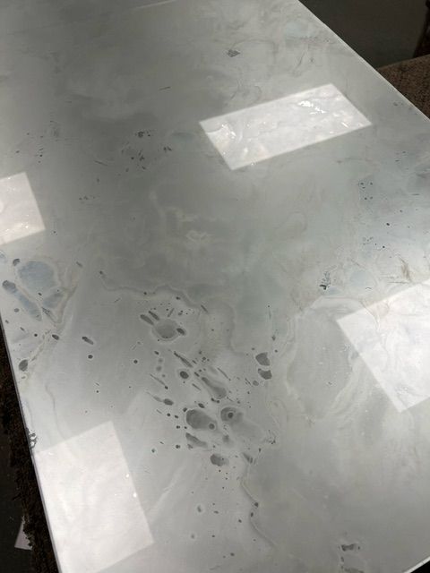 A white countertop with smudged, cloudy, and spotty surface markings reflecting light.