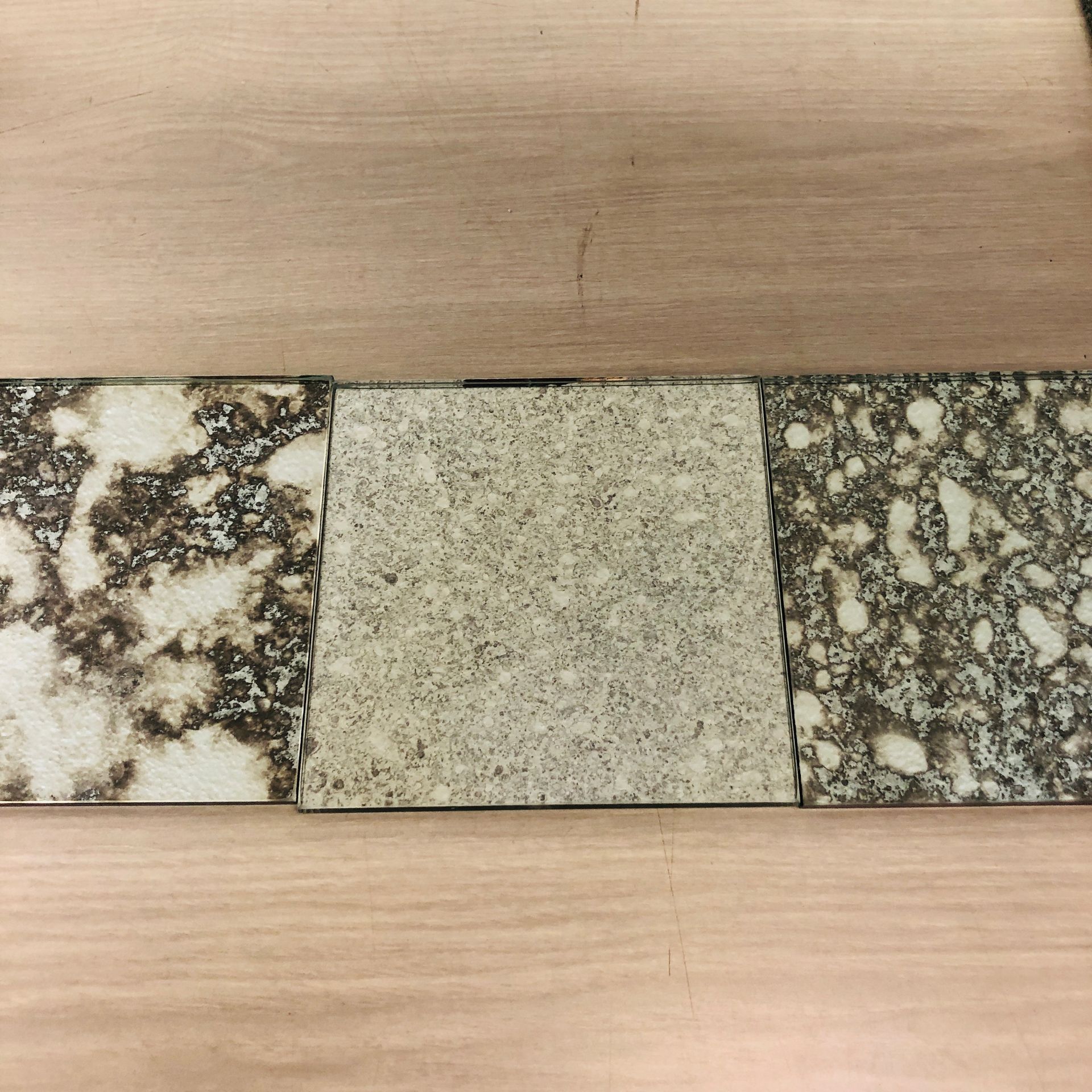 Three square tiles with varying textures and shades of gray, brown, and cream, displayed side-by-side on a light wood surface.