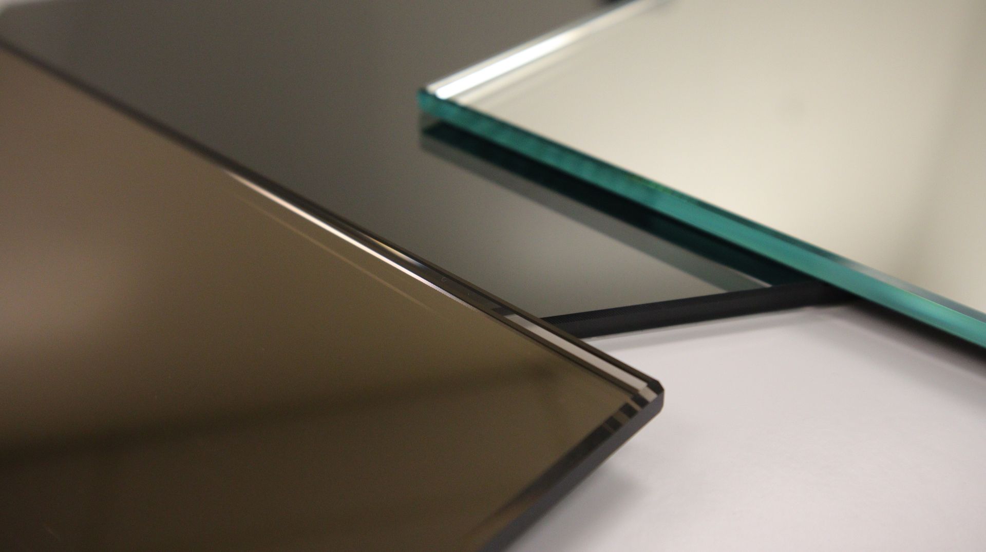 A close-up view of three stacked glass sheets, featuring a bronze-tinted, a black-tinted, and a clear reflective piece.