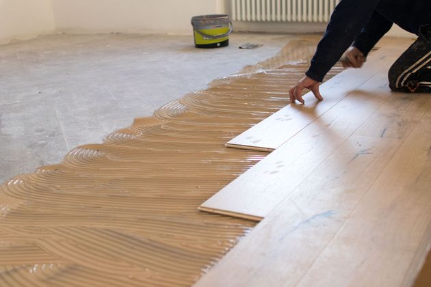 Person spreading adhesive on a floor and laying white tiles in a room under renovation