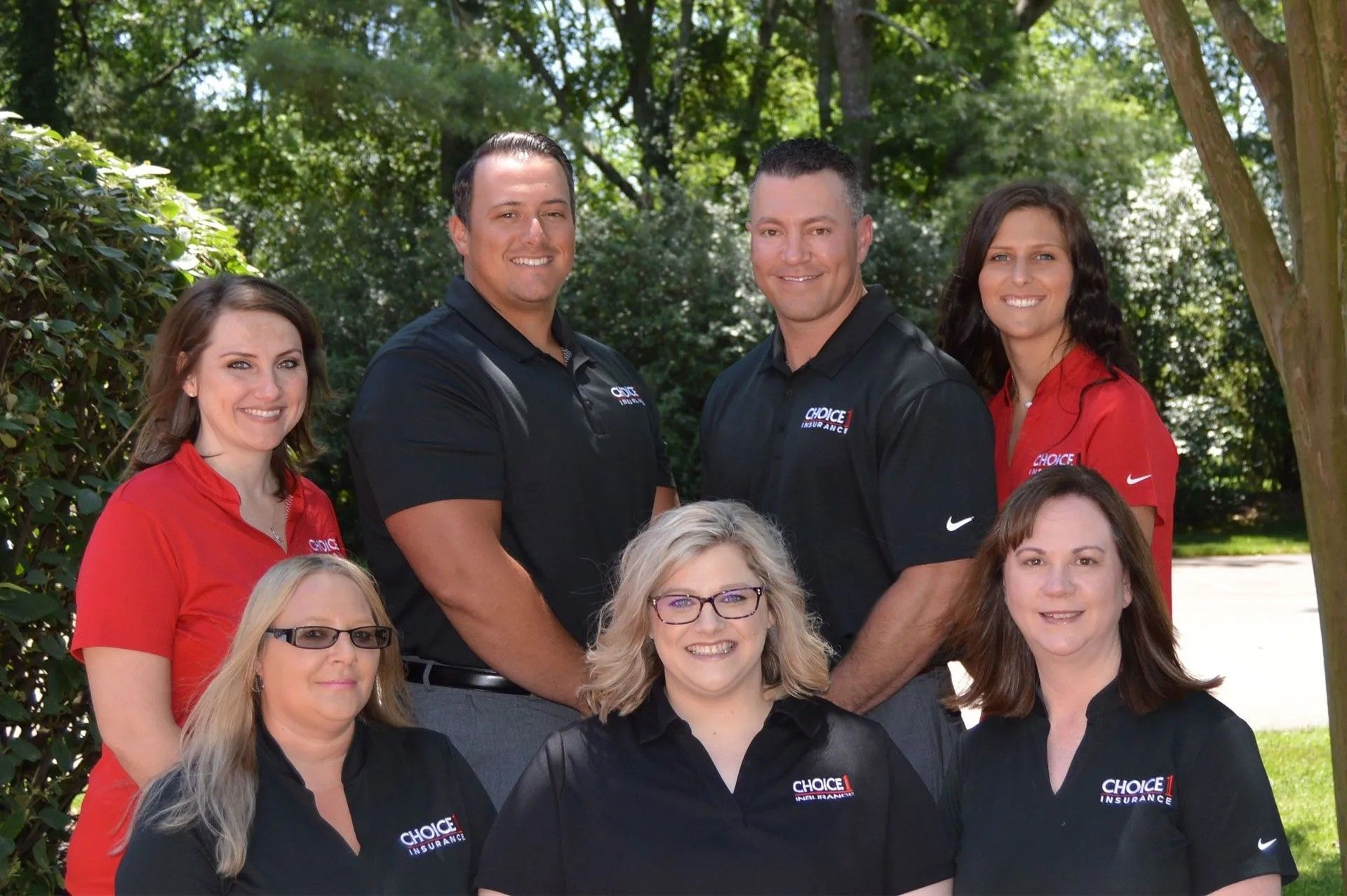Group of seven people posing outdoors; all are wearing company logo shirts.