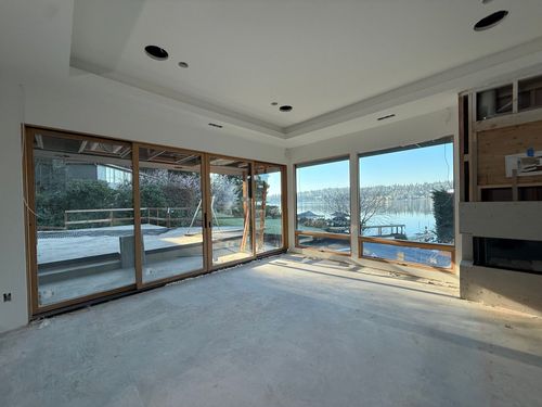 Bright empty living room with large glass doors opening to a sunny waterfront view.