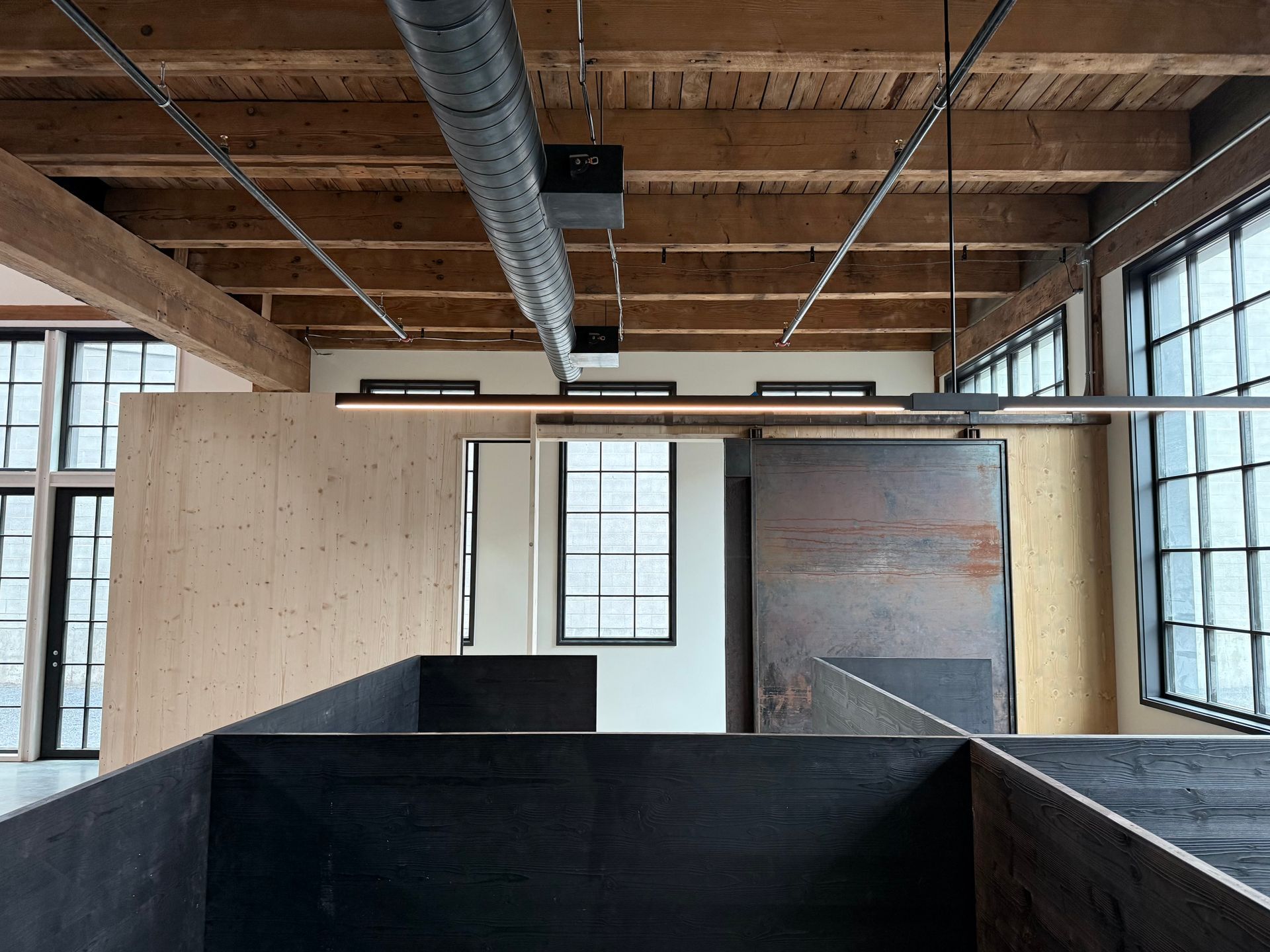 Industrial loft interior with exposed beams, ductwork, large windows, and black partition walls