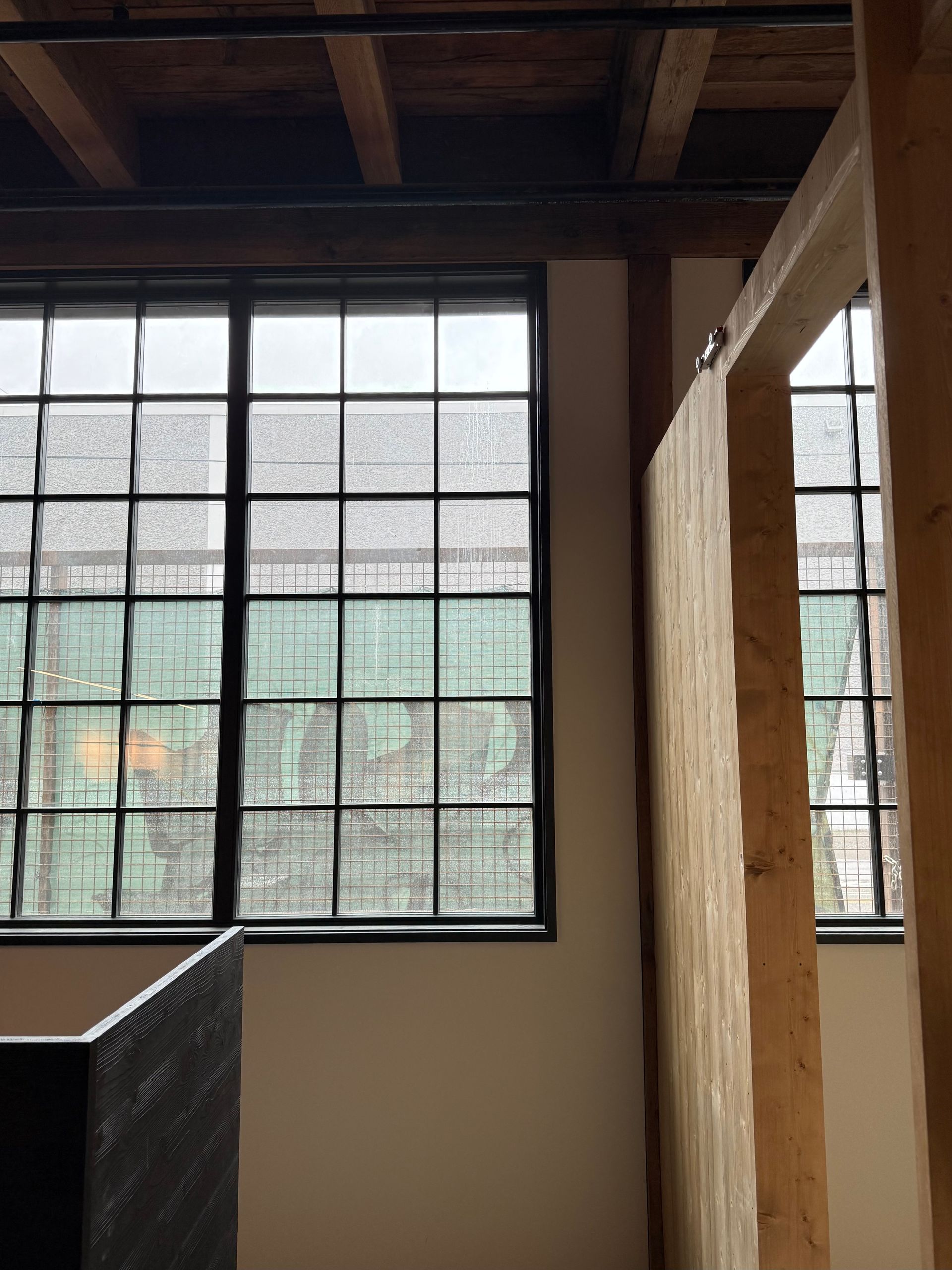 Interior with large gridded windows, exposed wooden beams, and a hanging curtain by a staircase.