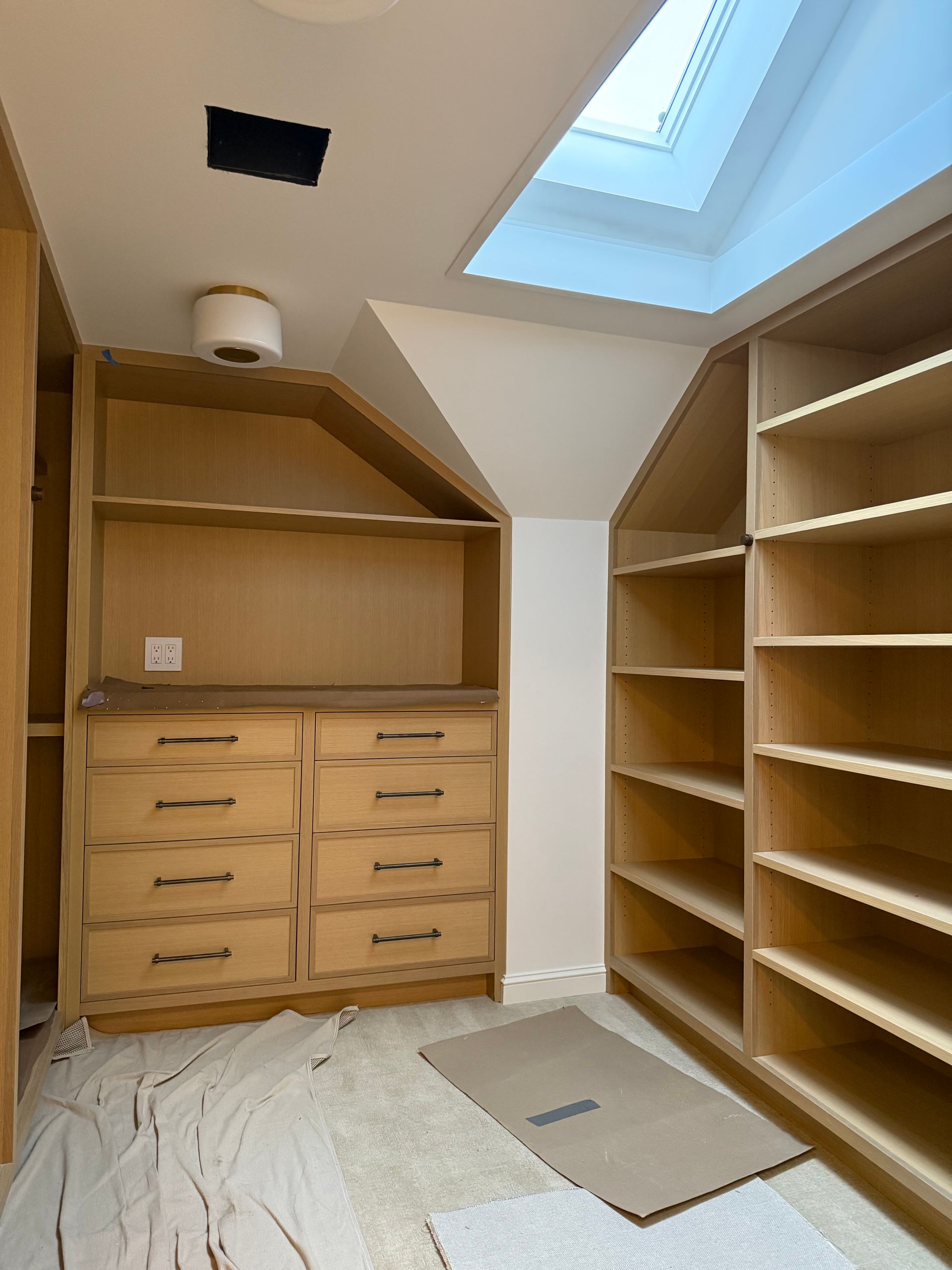 Walk-in closet with wood shelving, drawers, and a skylight, unfinished floor area in the center.