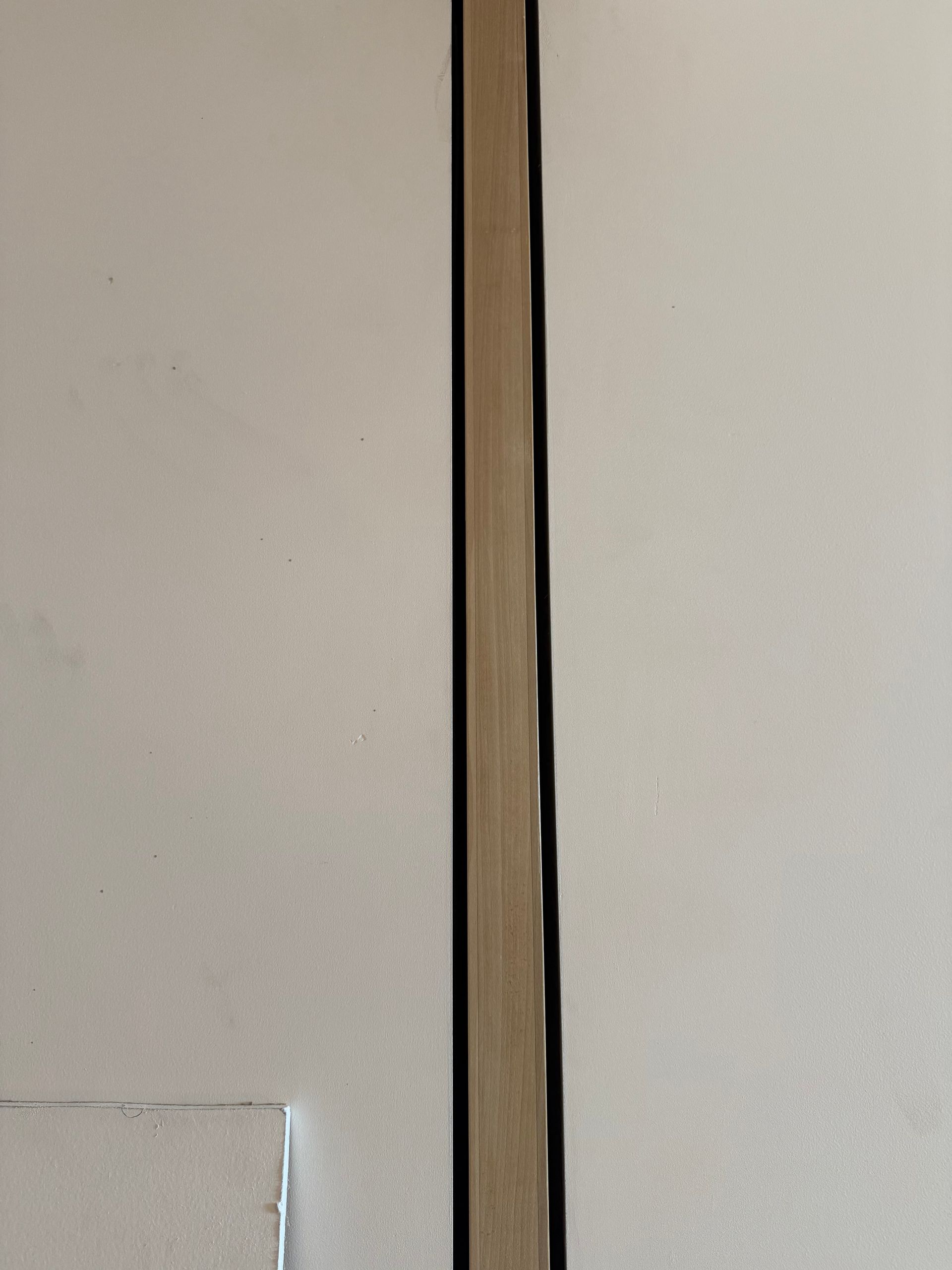 Close-up of a vertical wooden strip between two white walls with a small chipped corner at bottom left