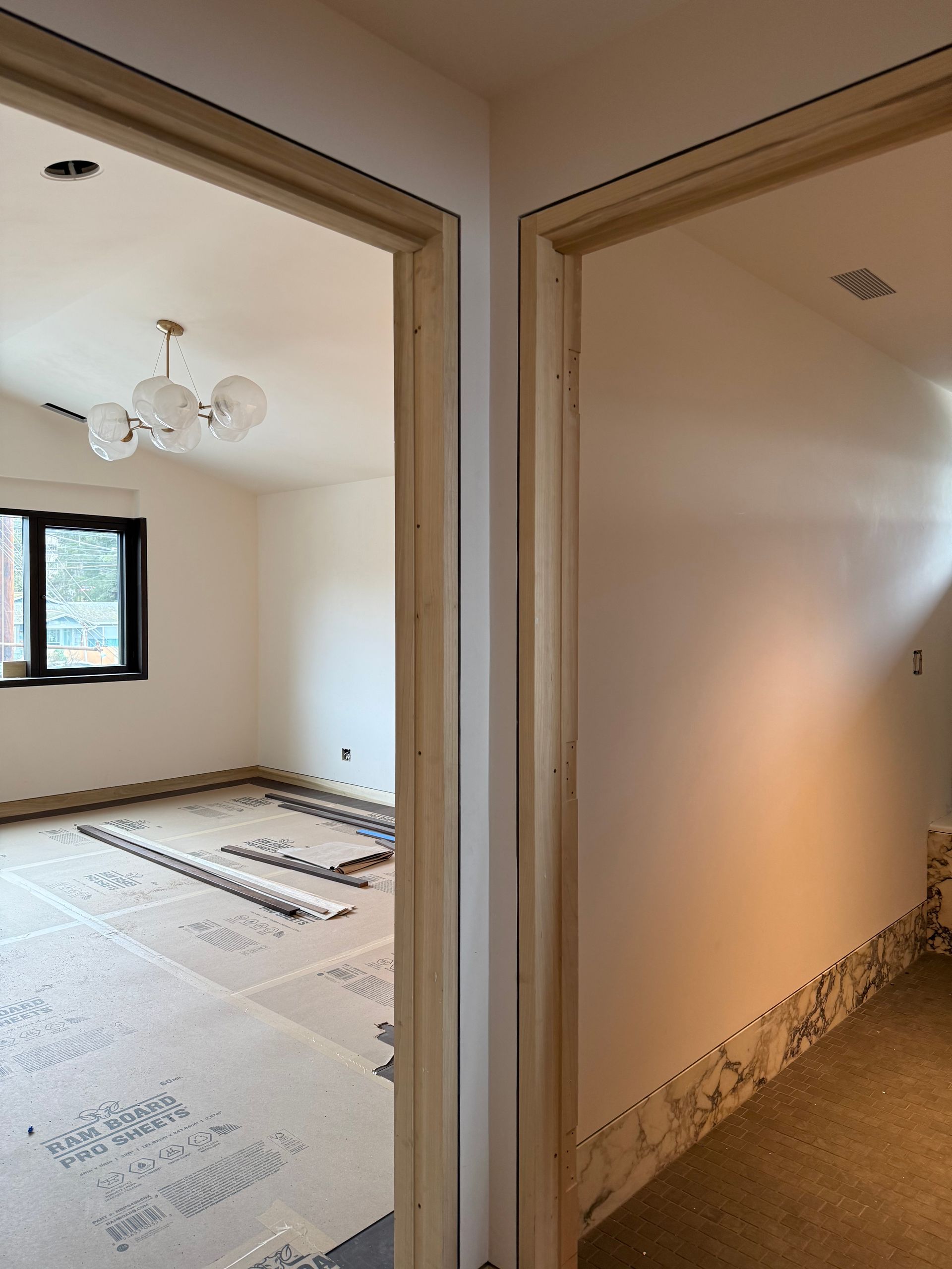 Hallway view into two empty rooms under renovation, with white walls, beige floors, and windows.