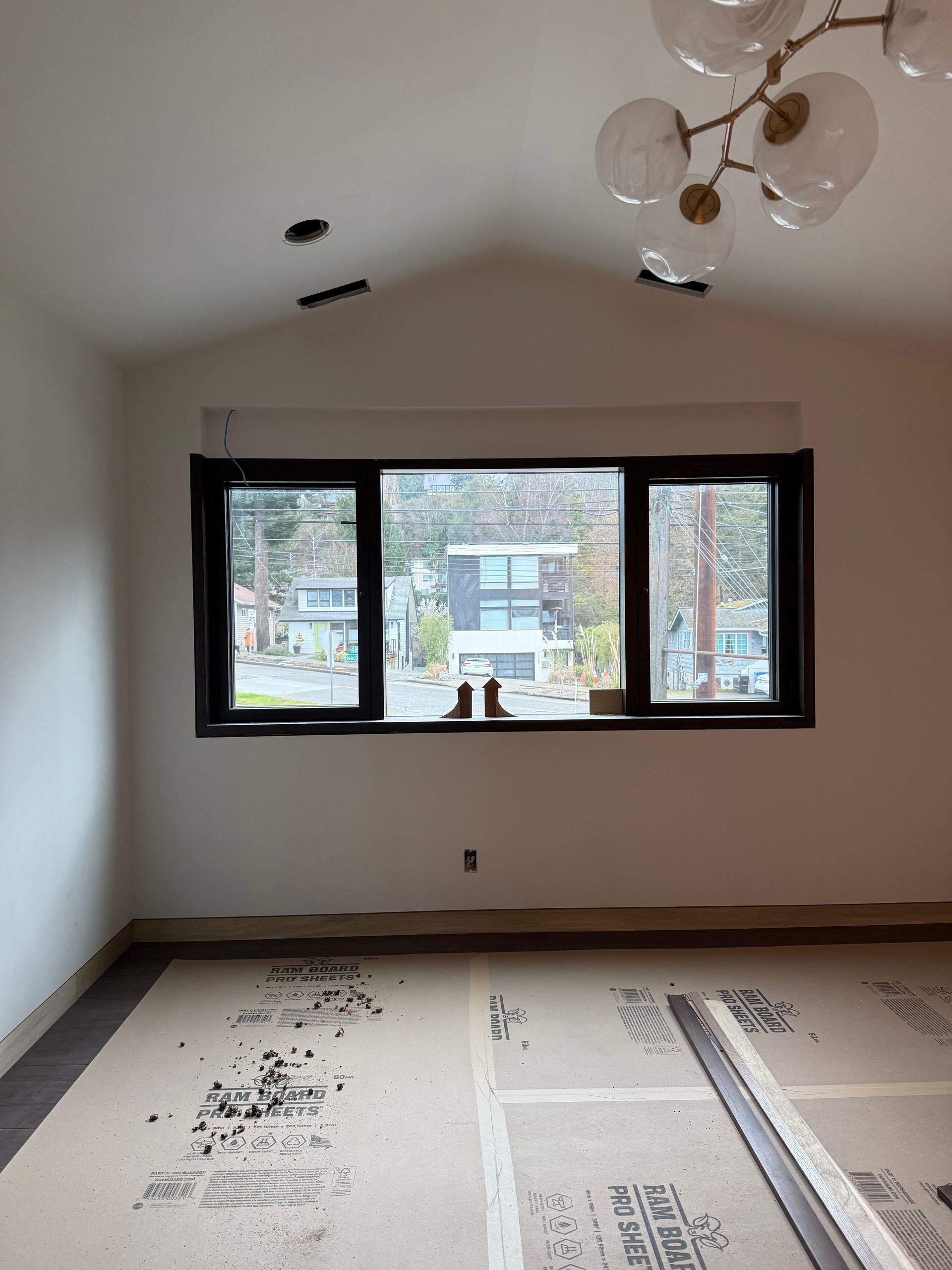 Empty room with white walls, black-trimmed window, and exposed flooring during renovation.