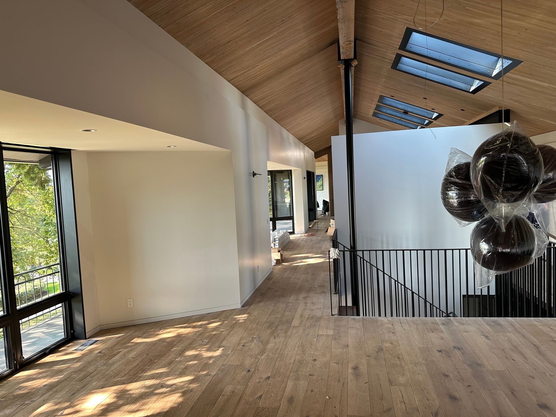 Modern loft interior with wood ceiling, skylights, glass railings, and sunlight on wooden floors