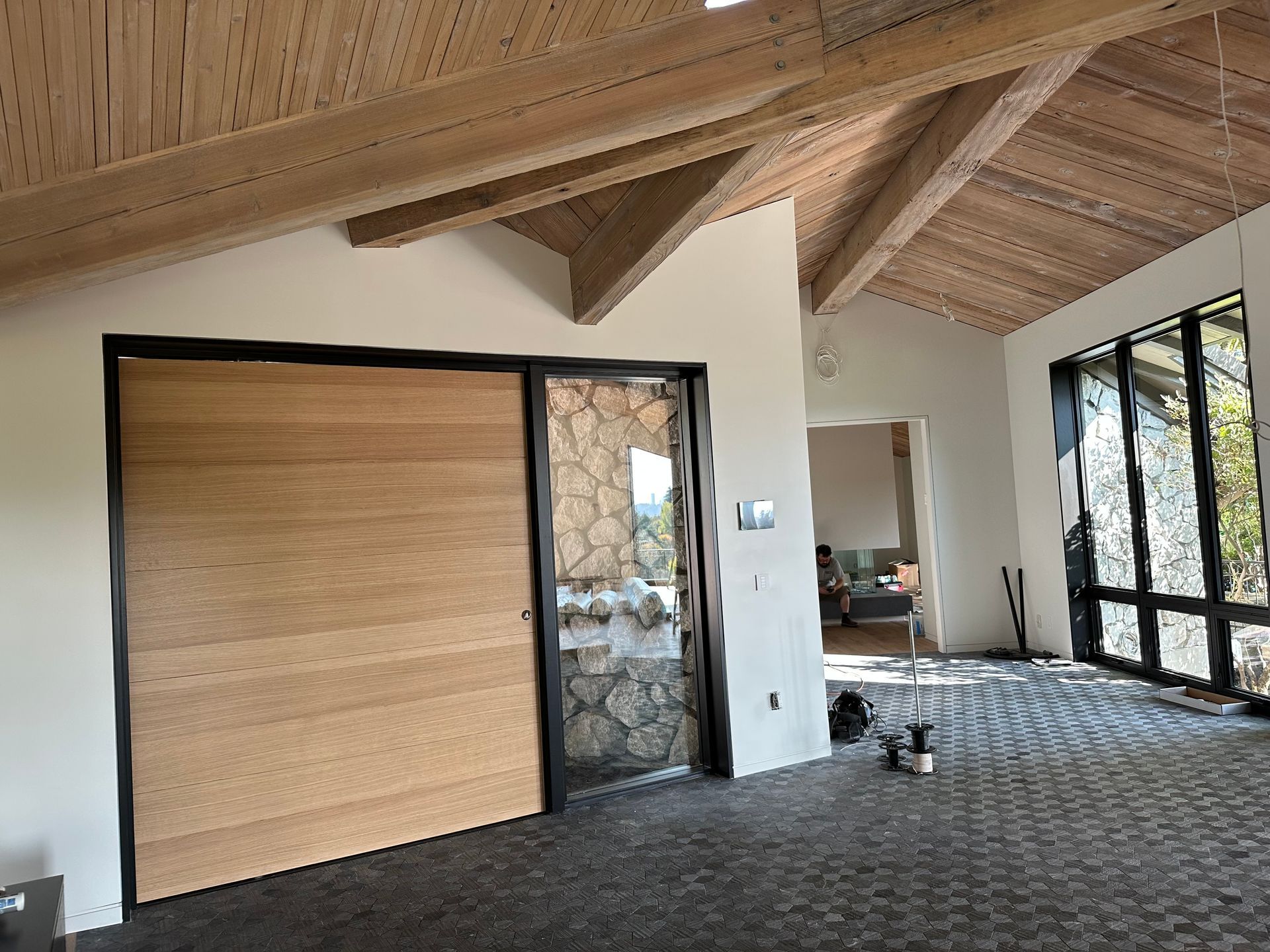 Modern interior with wood ceiling, large sliding door, stone wall, and patterned floor, lit by daylight