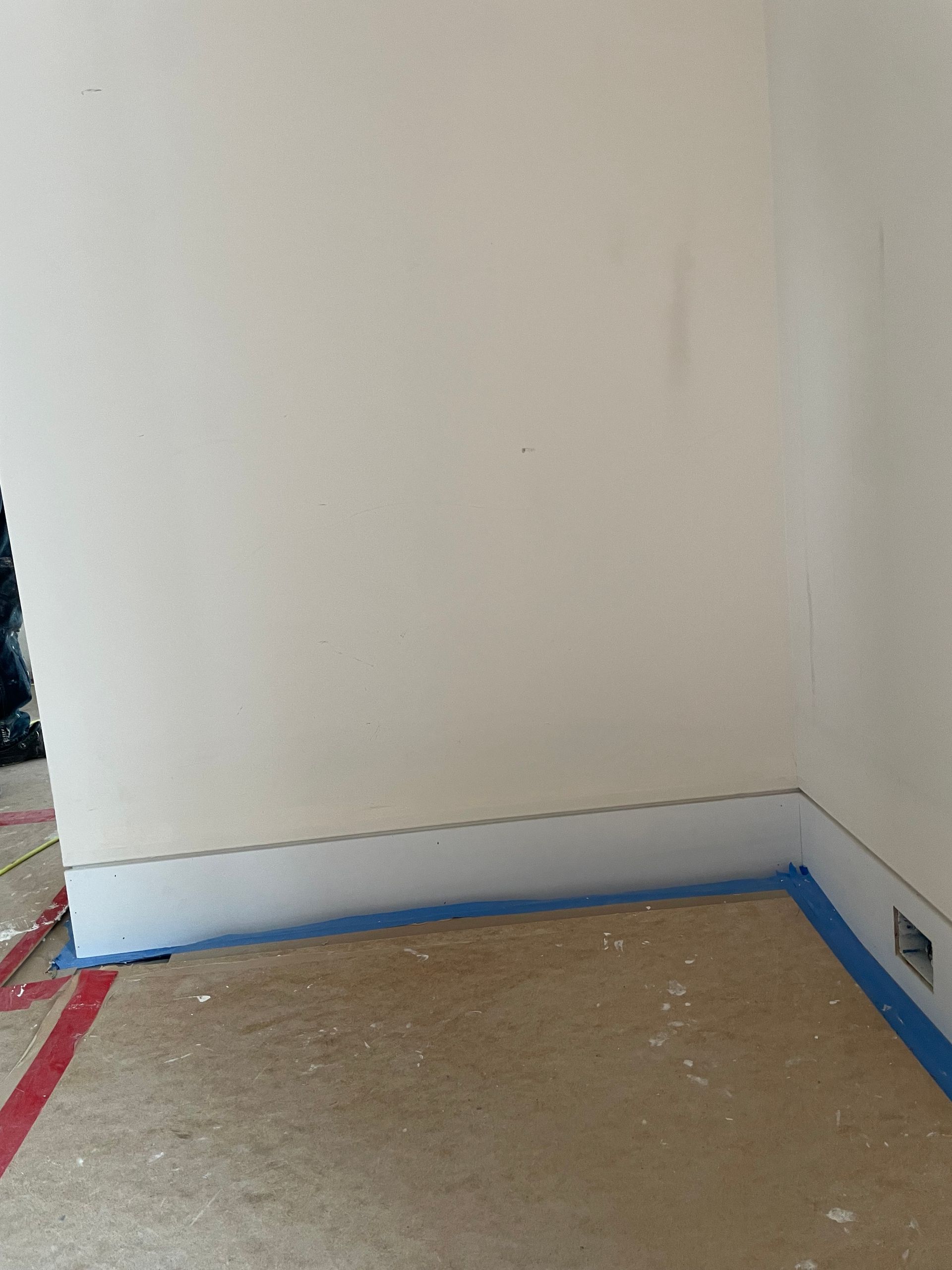 Empty room corner with white walls, blue baseboard, and bare floor under renovation