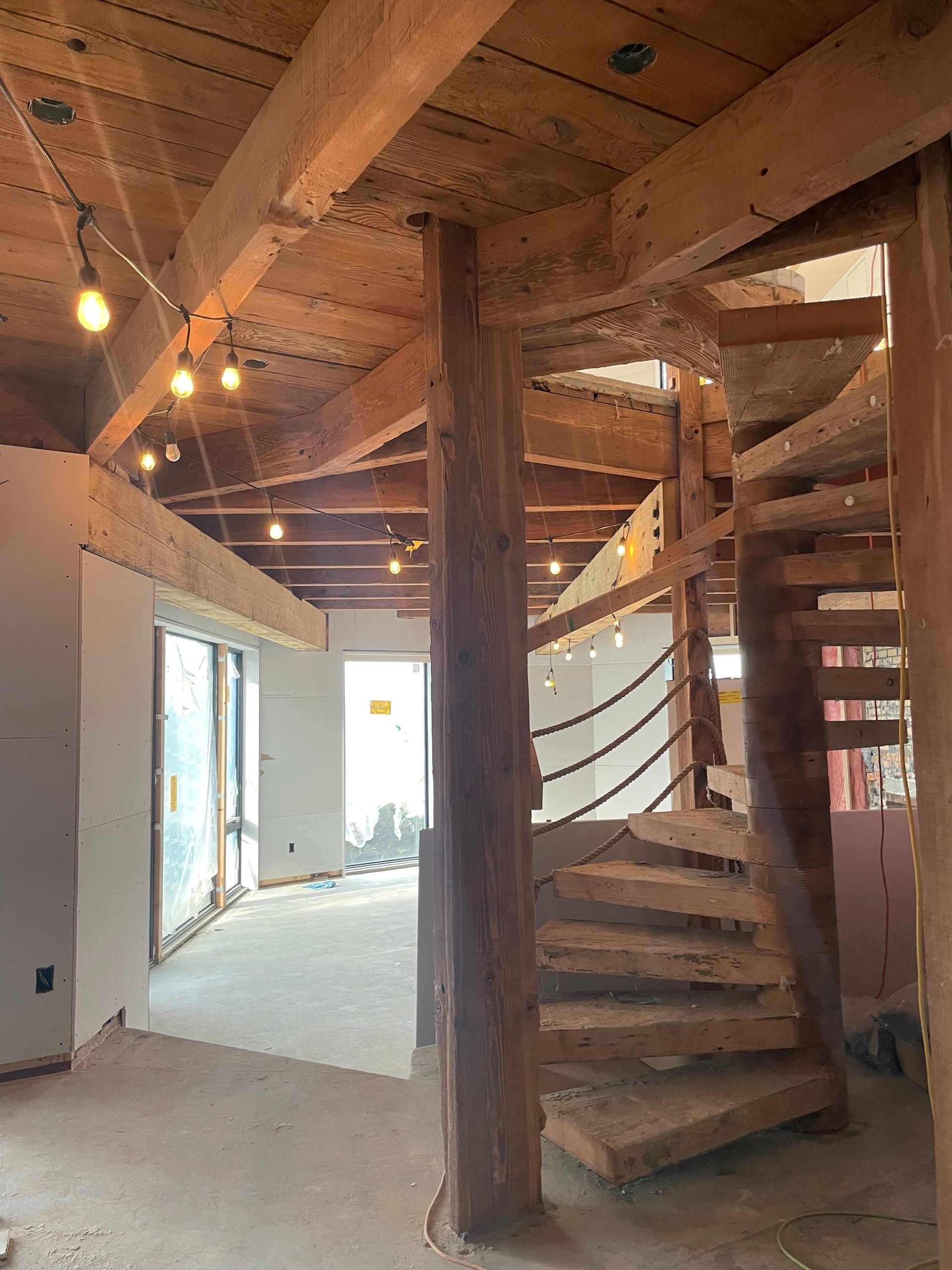Interior of a rustic cabin with exposed wood beams, a spiral staircase, and unfinished walls.