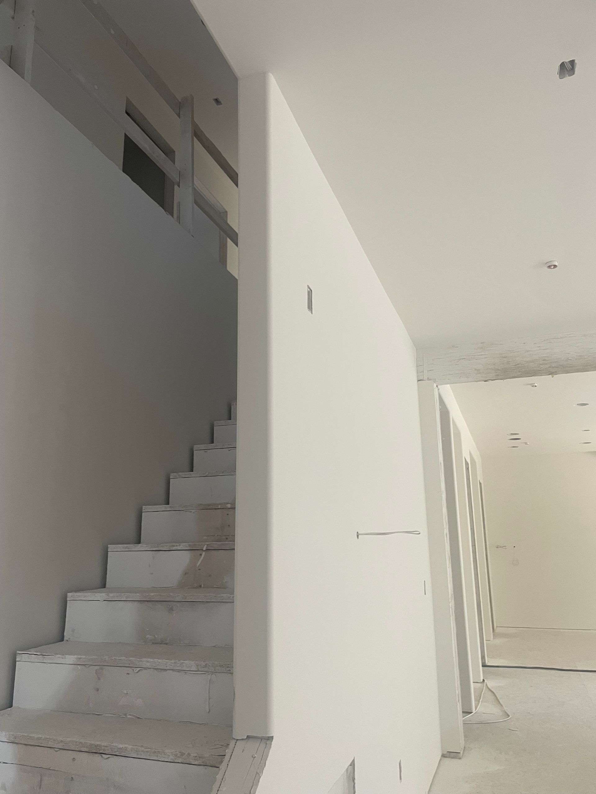 White interior stairwell with unfinished walls and stairs leading up to a landing
