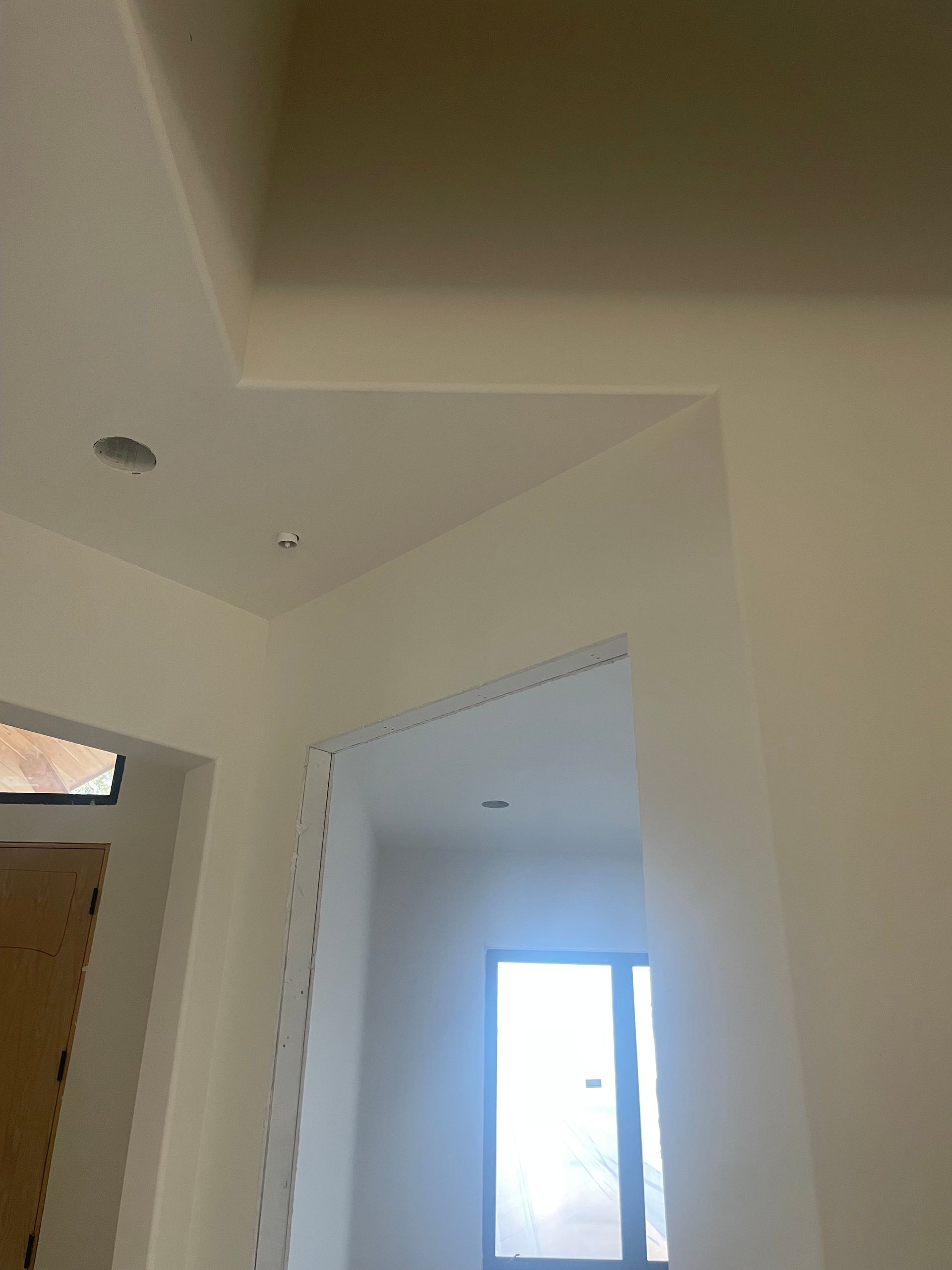 Indoor hallway with white walls and ceiling, open doorway, and a bright window in the background