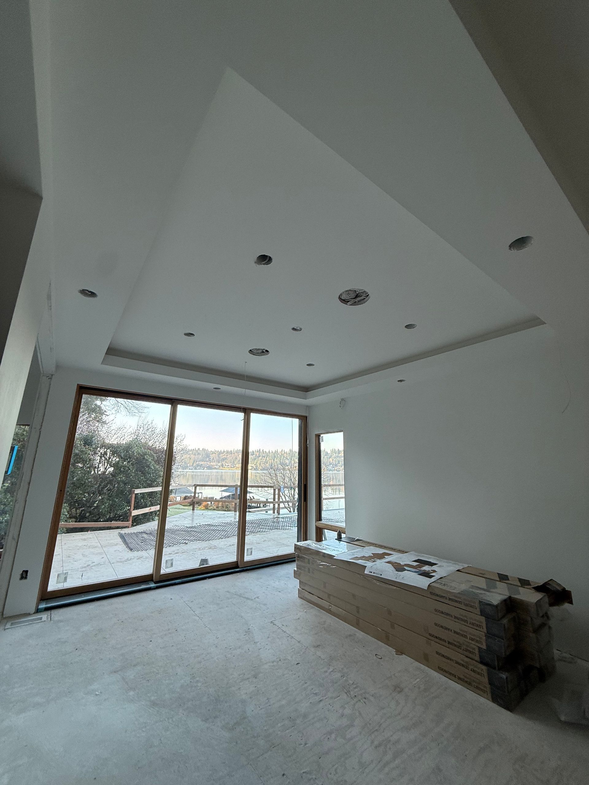 Empty modern living room under renovation with large sliding glass doors and recessed ceiling lights