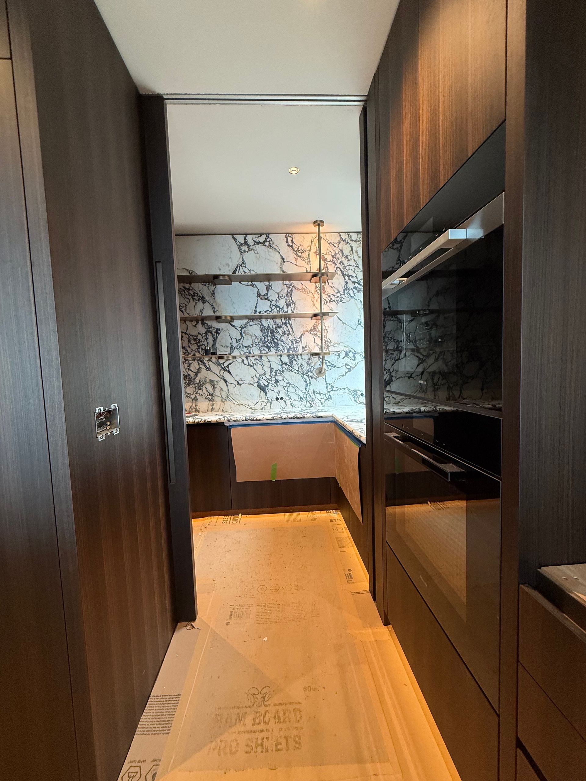 Narrow modern hallway with dark wood cabinets, patterned glass, and a small desk at the far end.