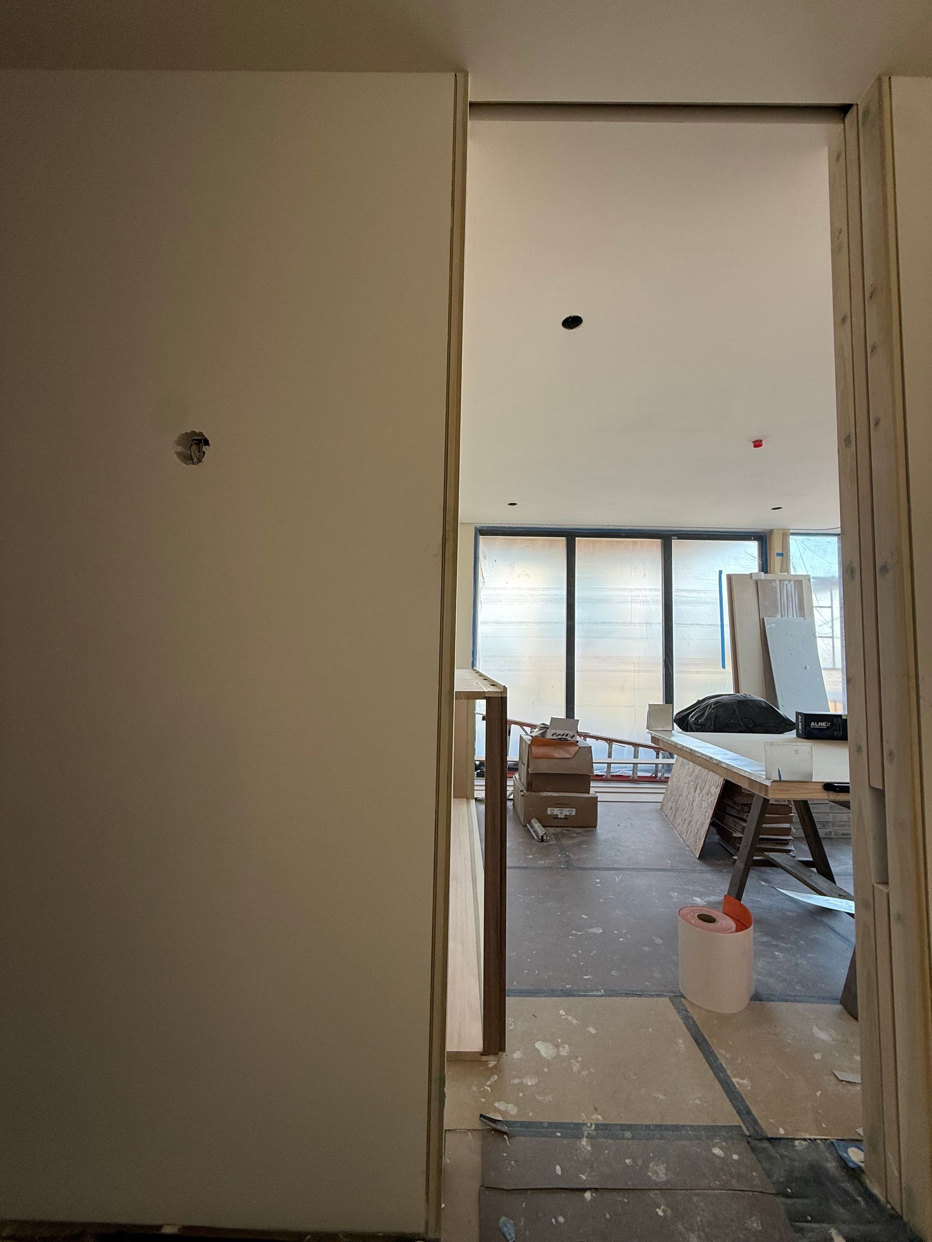 Unfinished interior with open doorway, scattered construction materials, and sliding glass doors in the background