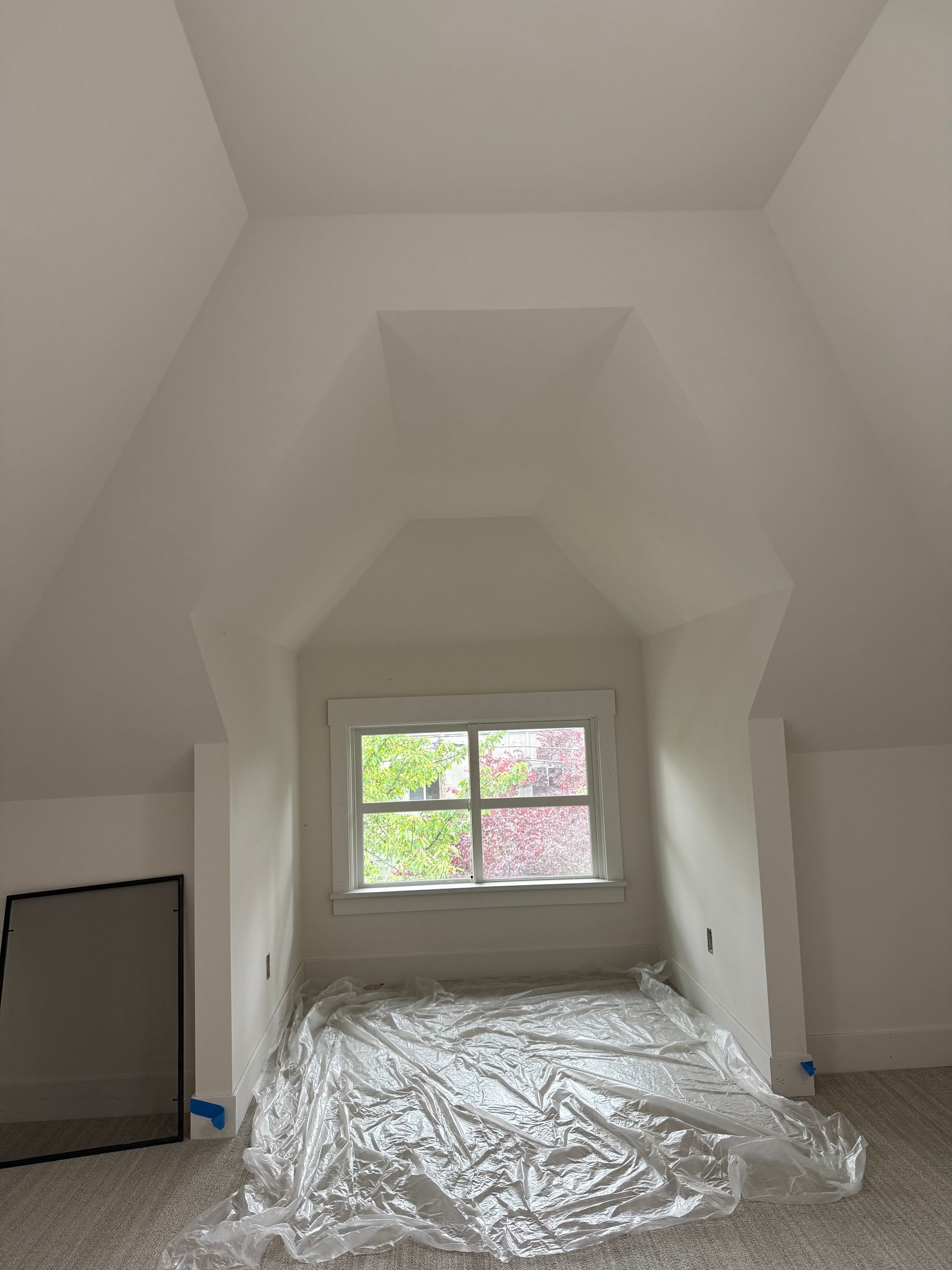 Attic room with sloped ceiling, small window, and plastic sheeting covering the floor.