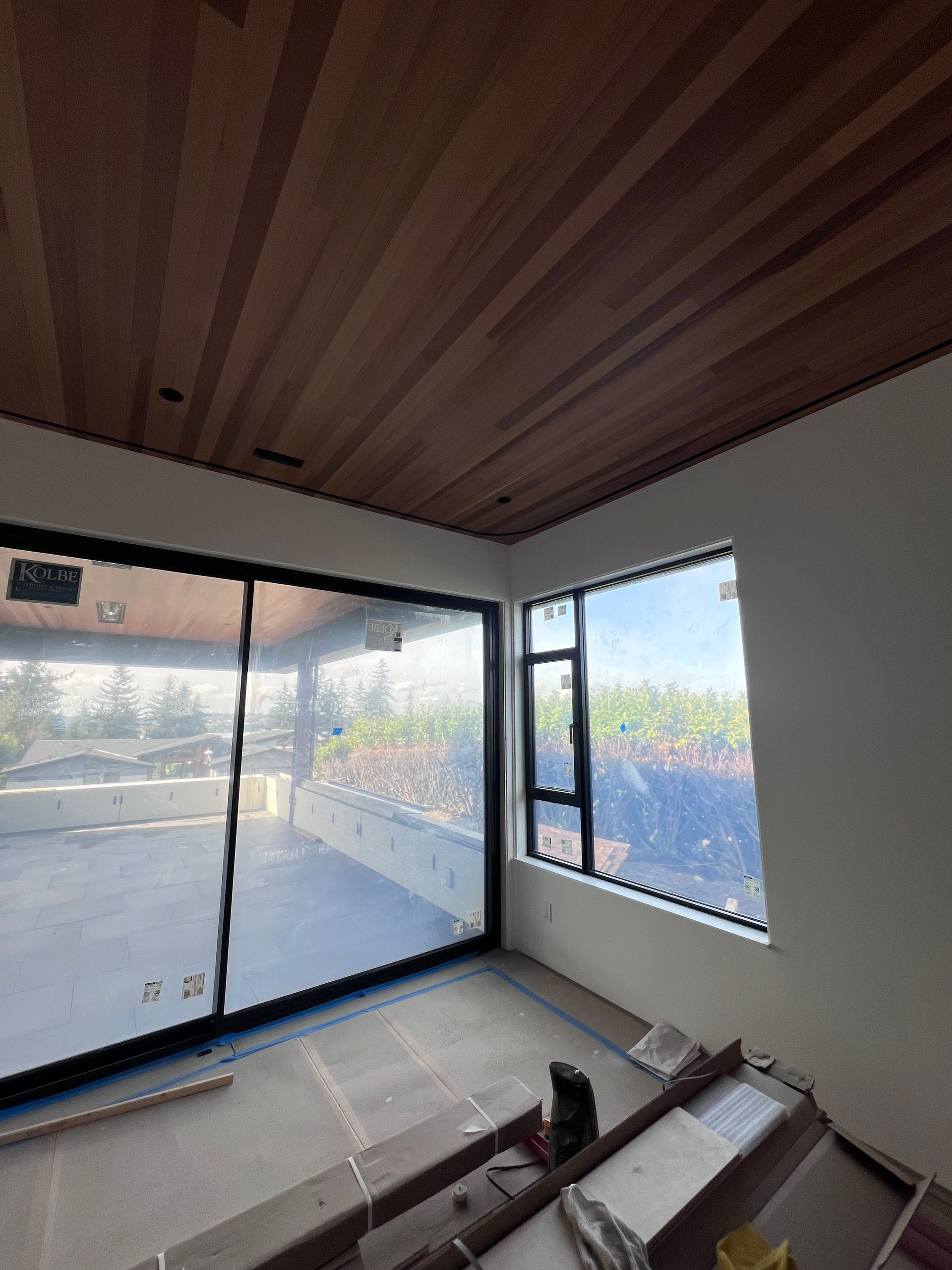 Empty room with wood ceiling, large windows, and stacked floor panels during renovation