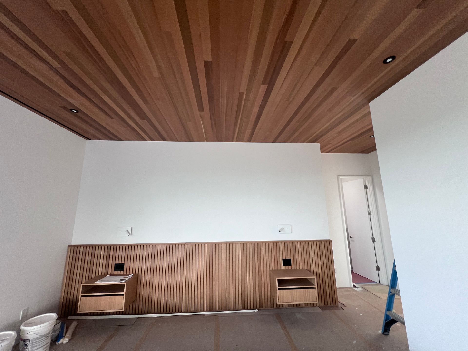 Modern room interior with slatted wood ceiling and wall paneling, white walls, and small wooden side tables
