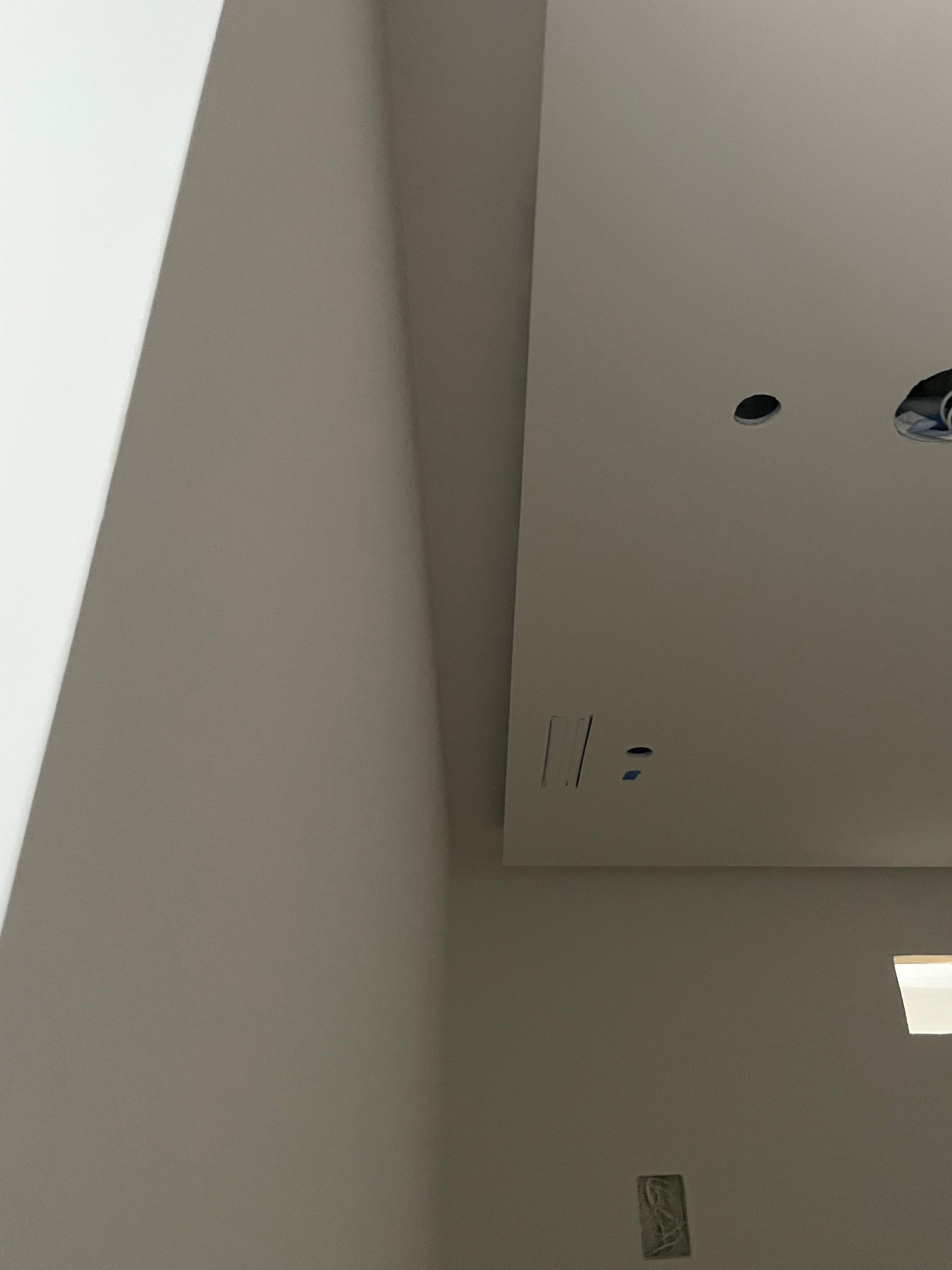 White interior ceiling corner with recessed light openings and wall vent under a slanted edge