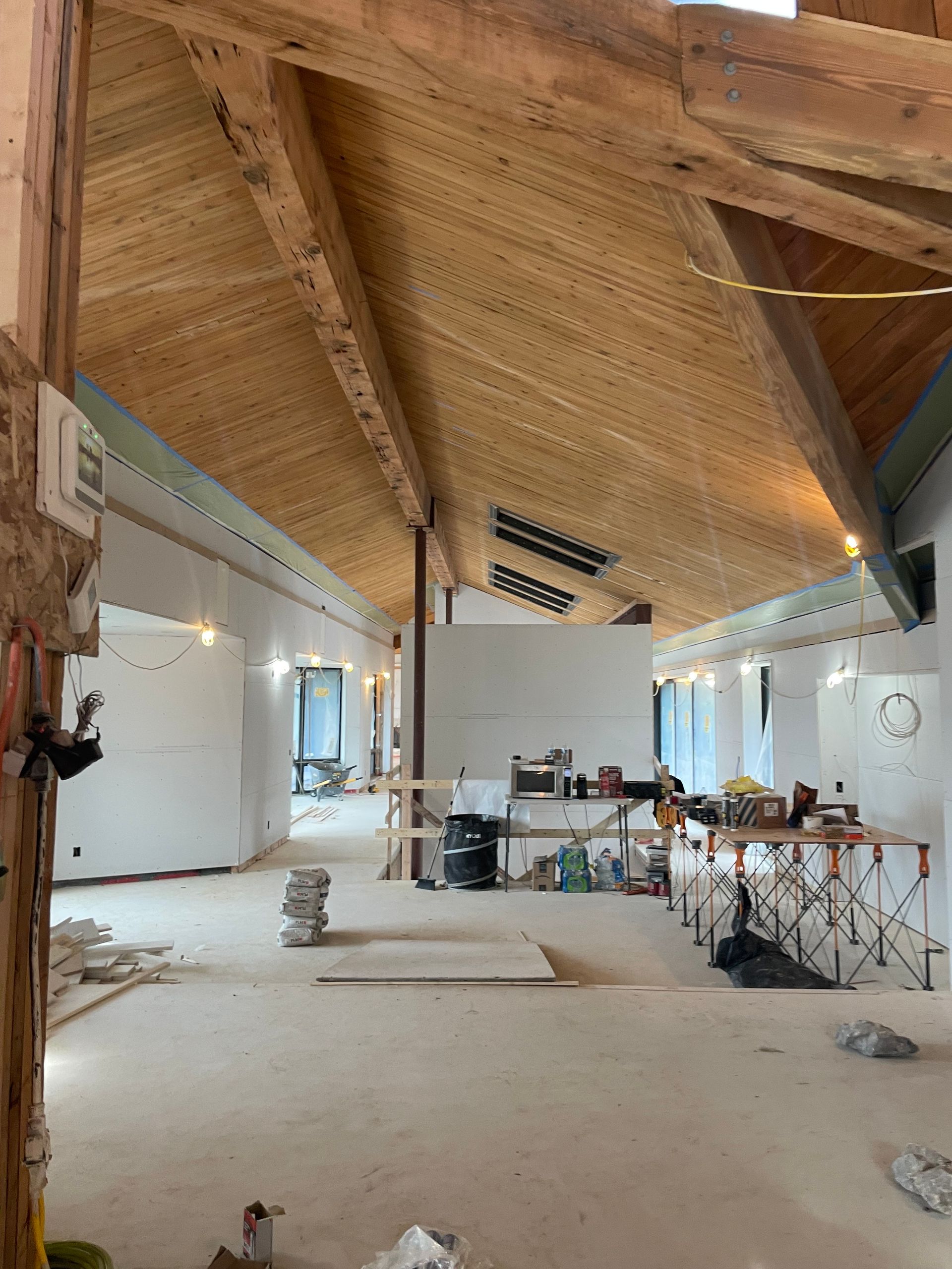 Bright unfinished interior with a high wooden vaulted ceiling, white walls, and construction materials scattered on the floor.