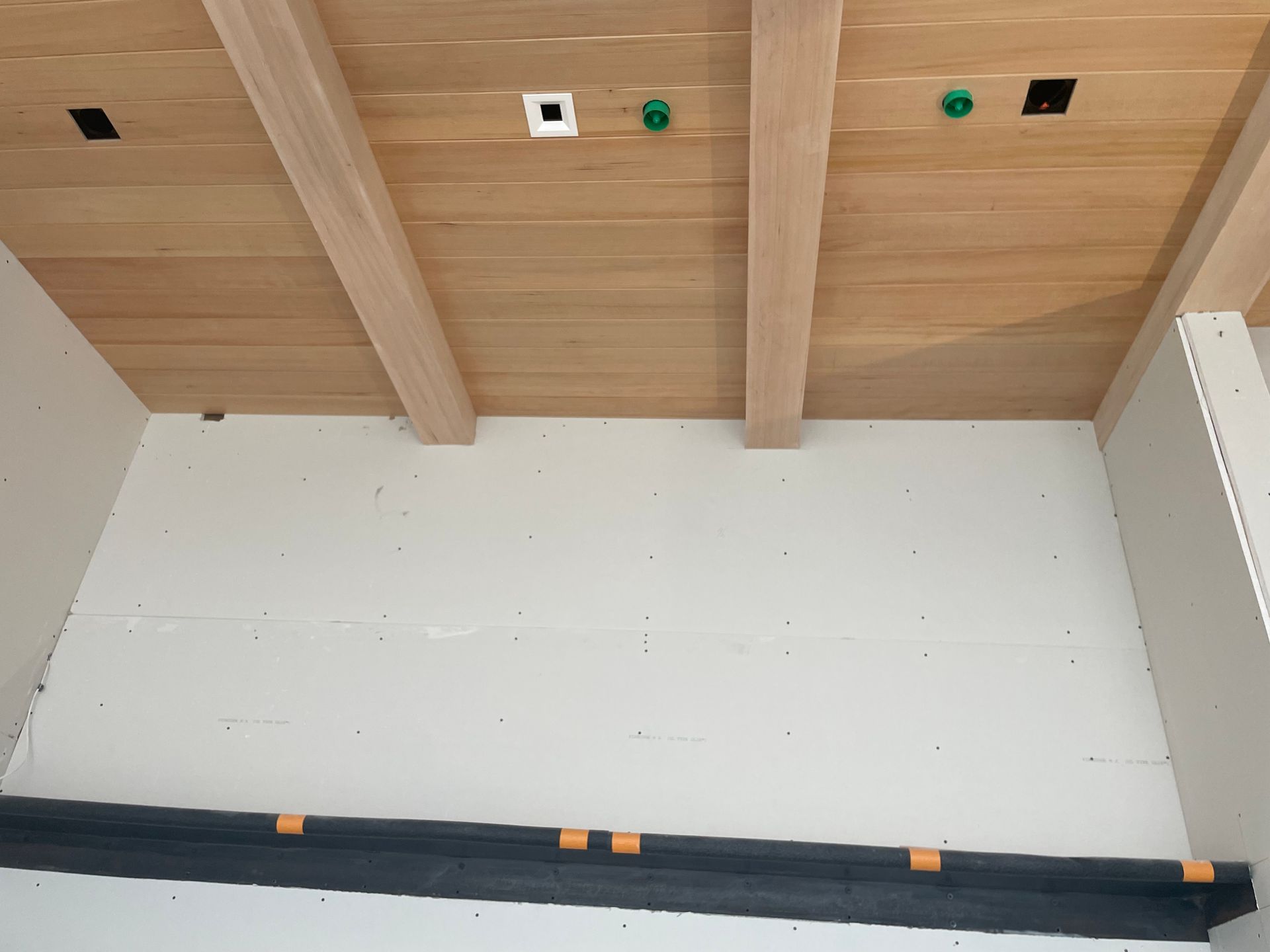 Empty room with wood-paneled ceiling, white walls, and exposed fixtures under construction