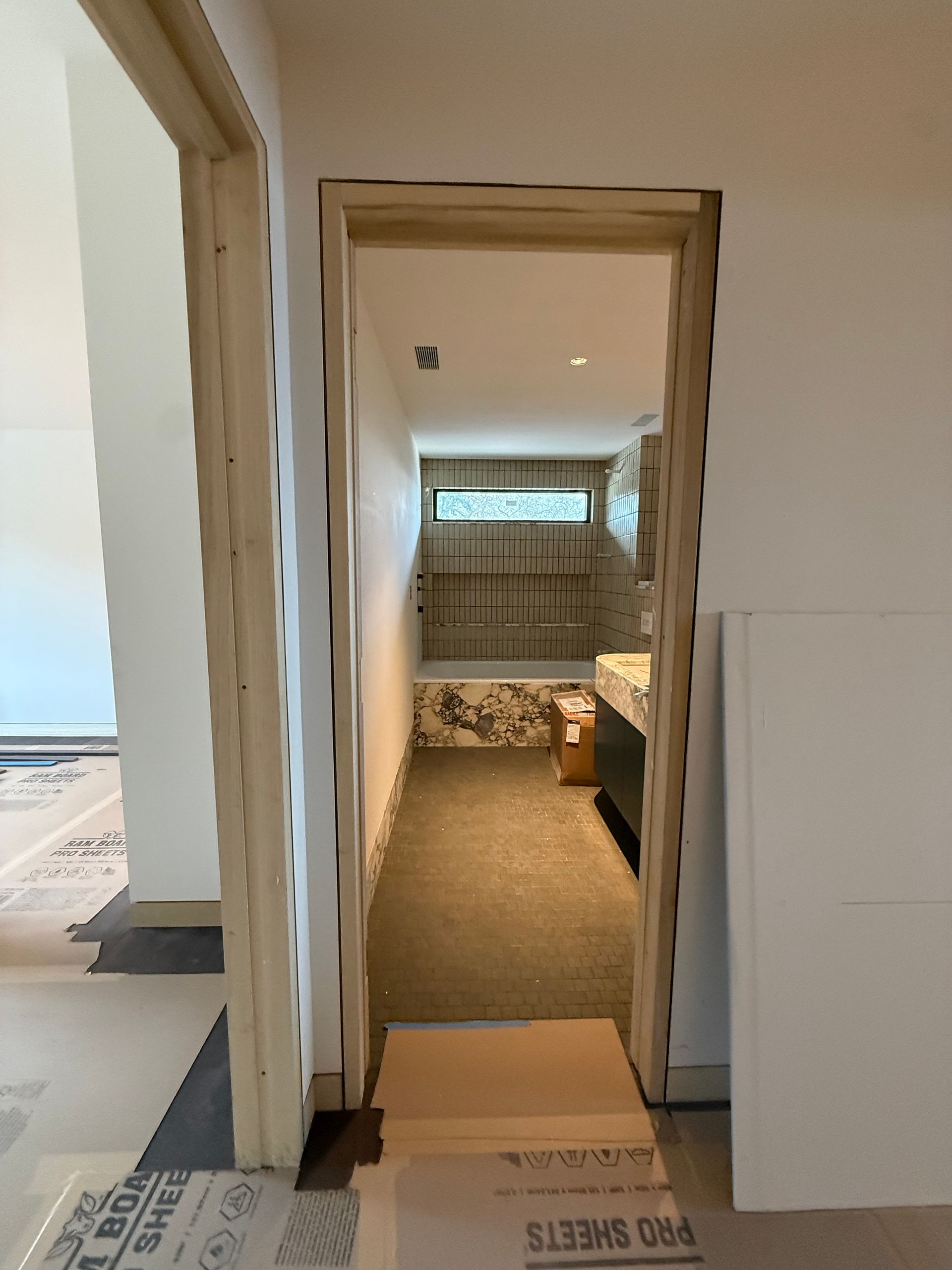 View through a doorway into a small bedroom with a bed, rug, and window at the far end.