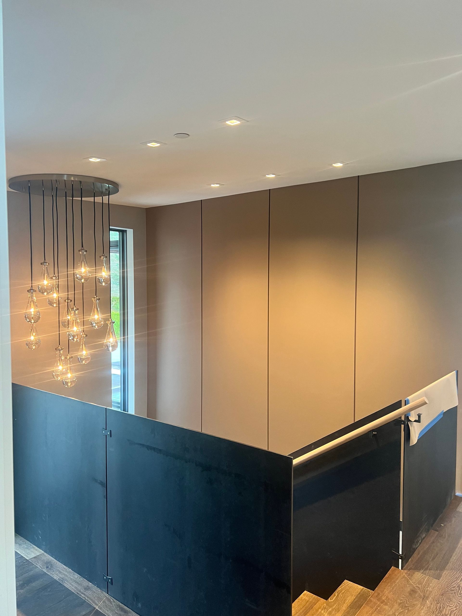 Modern hallway with dark glass railing, beige walls, and hanging chandelier lights