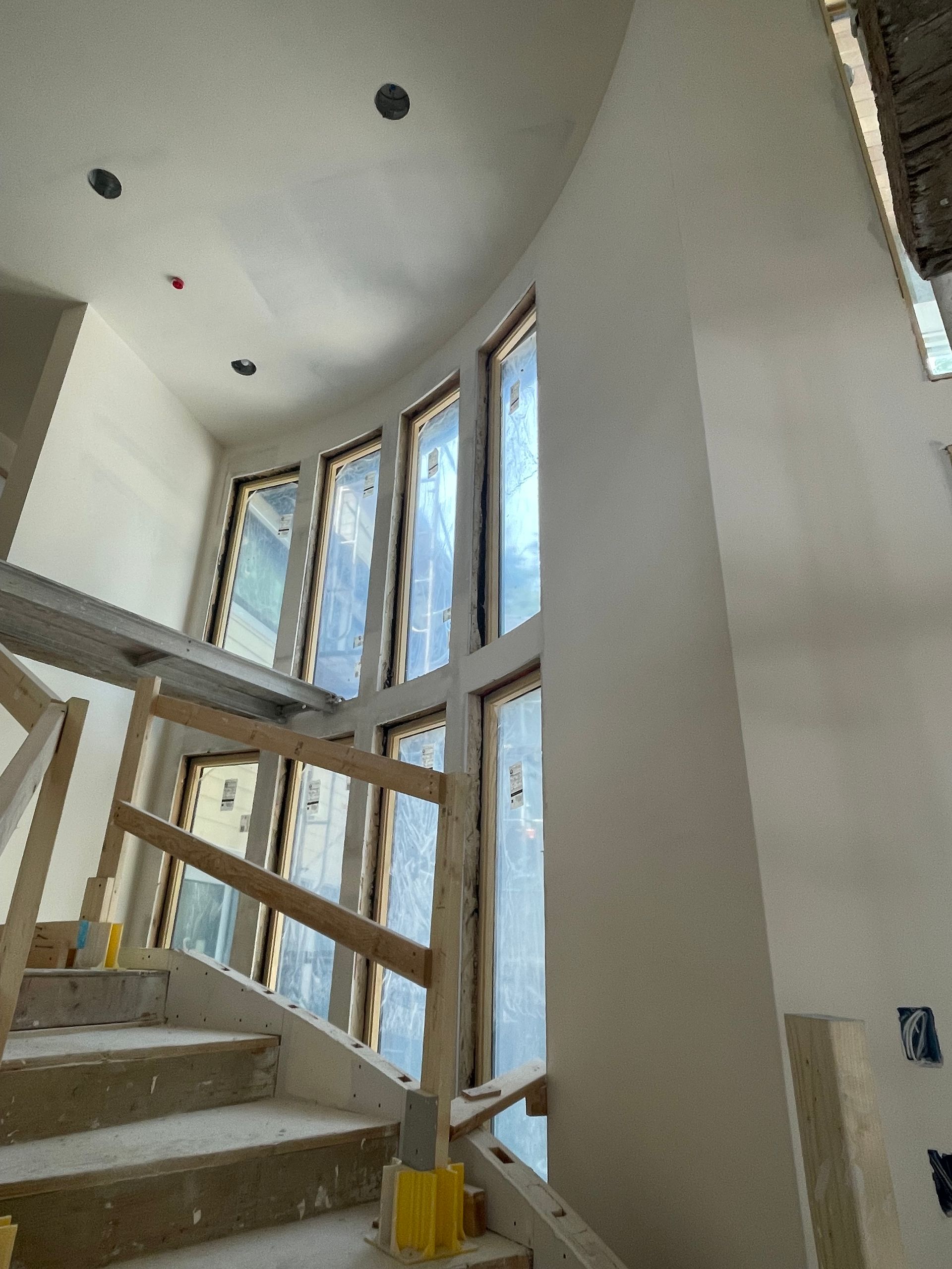 Interior stairwell with tall windows, white walls, and exposed wooden framing under construction