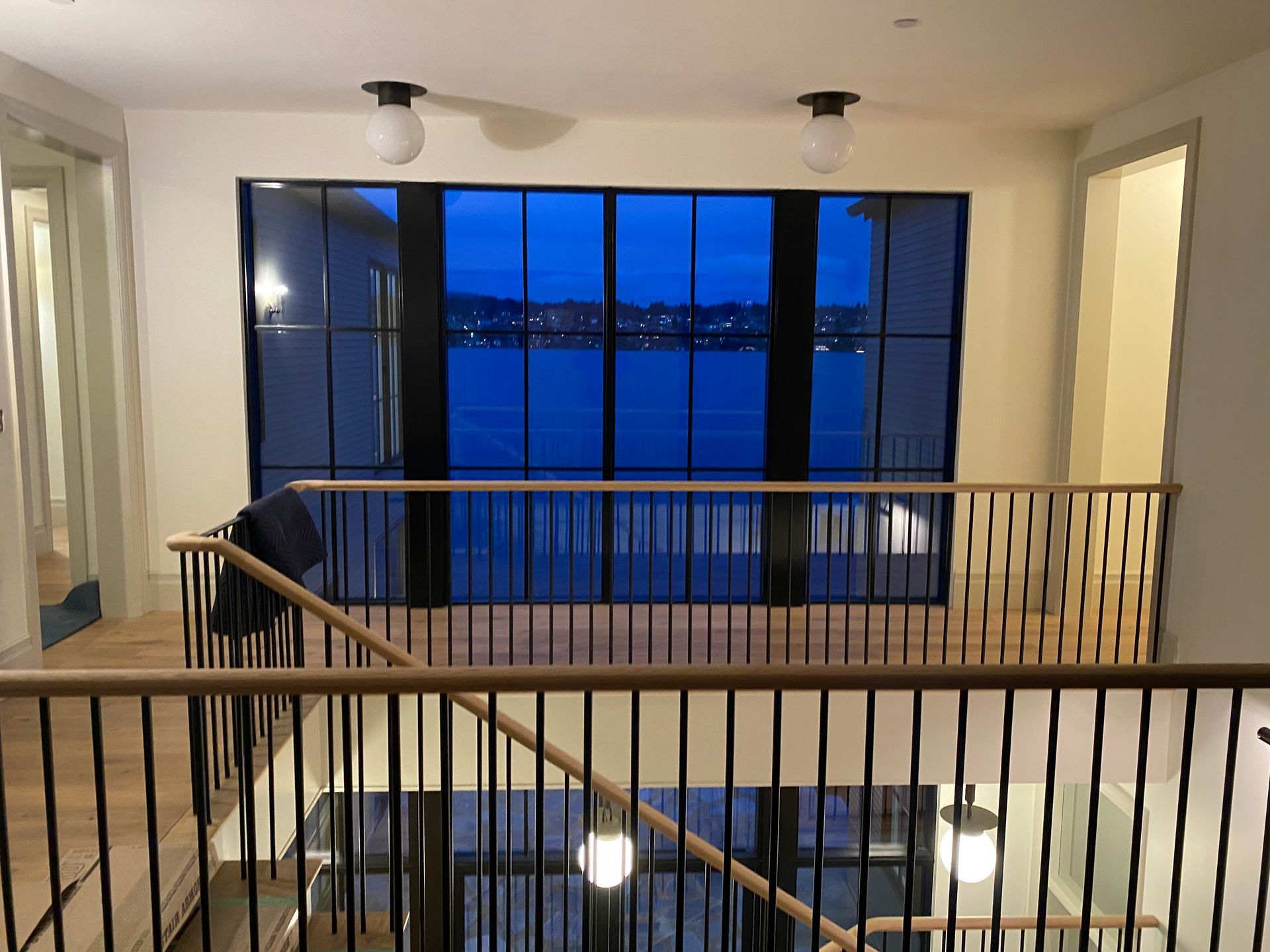 Modern interior landing with railing, framed by large windows overlooking a blue waterfront view at dusk