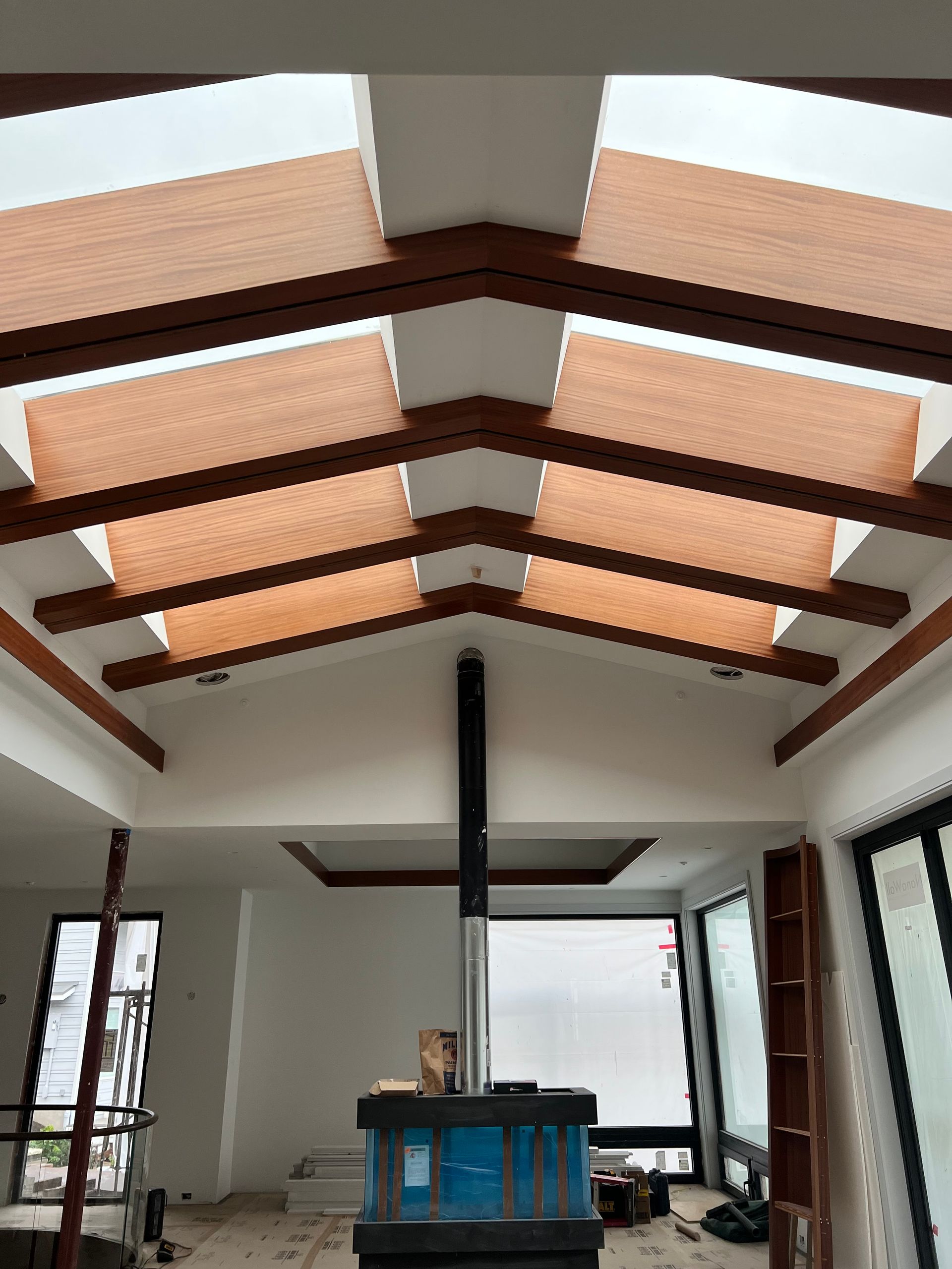 Interior of a room with exposed wooden beams, skylights, a central stove, and large windows.