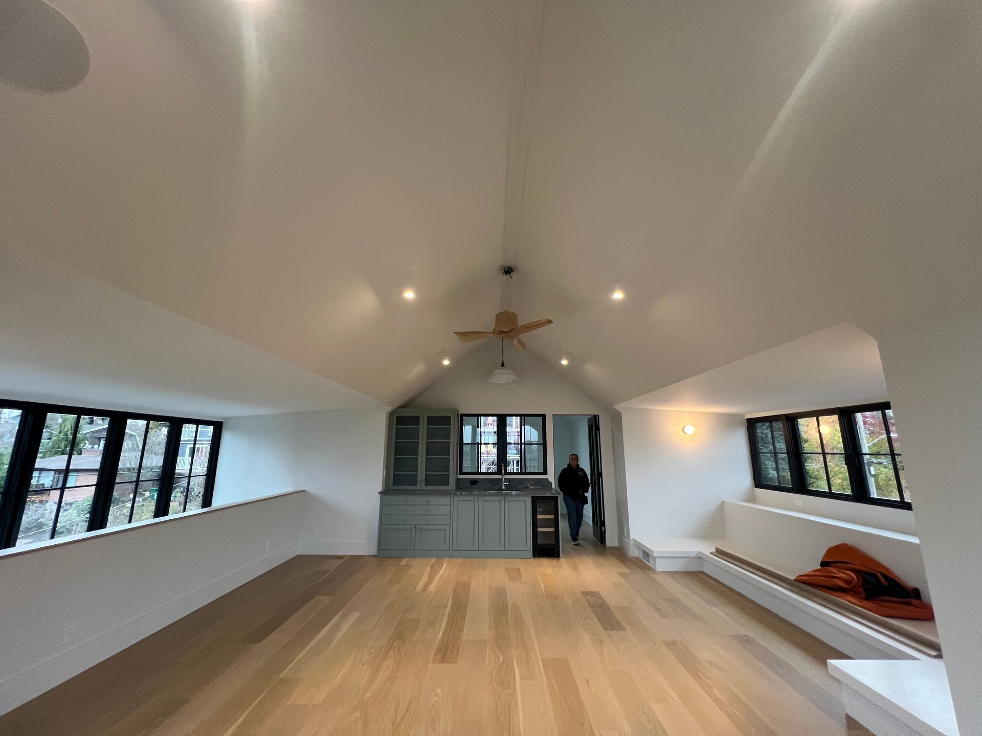 Spacious empty room with wood floor, white walls, long windows, and ceiling fan centered above.