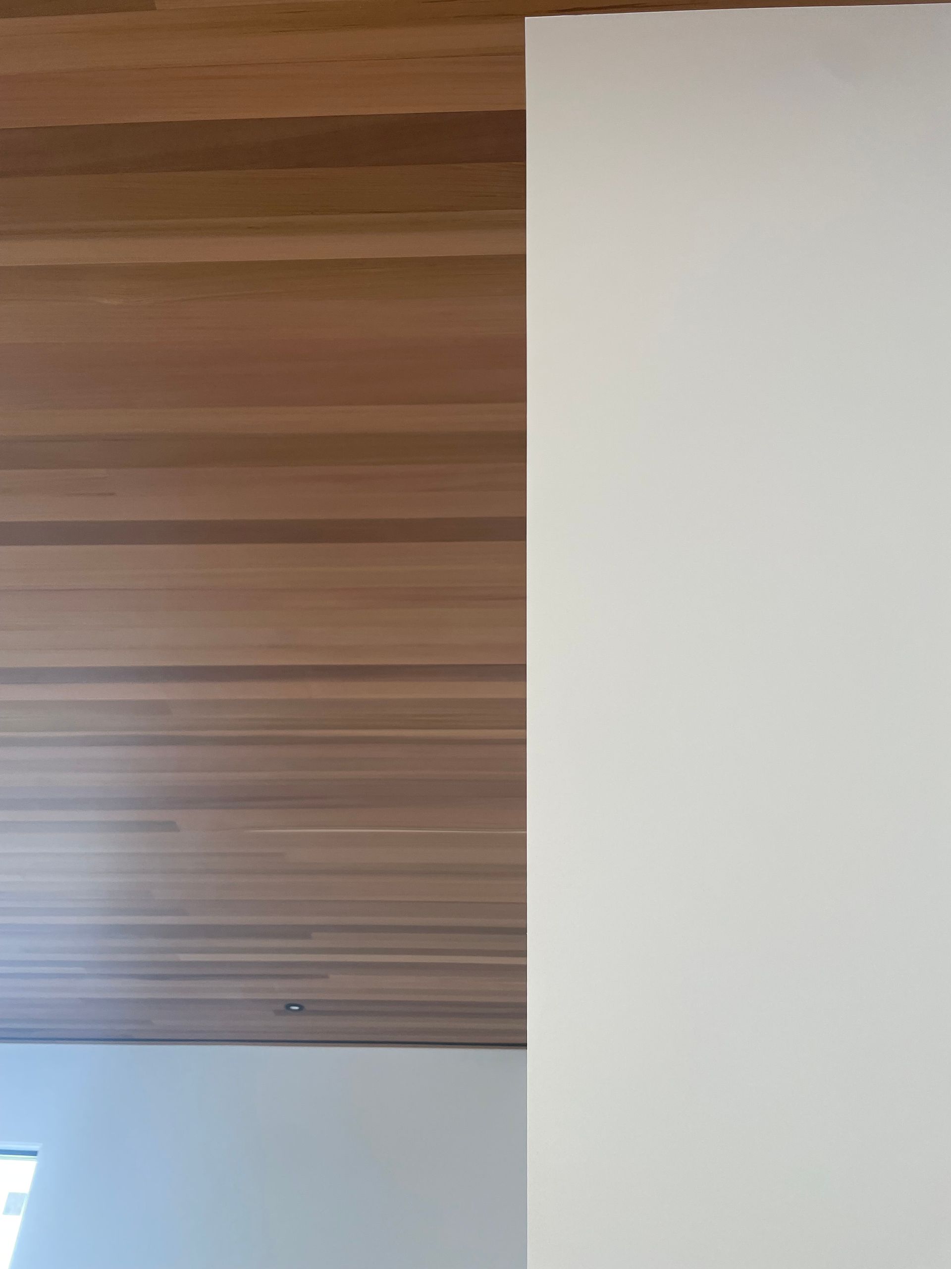 Wood-paneled ceiling above a white wall with a small window in the lower left corner
