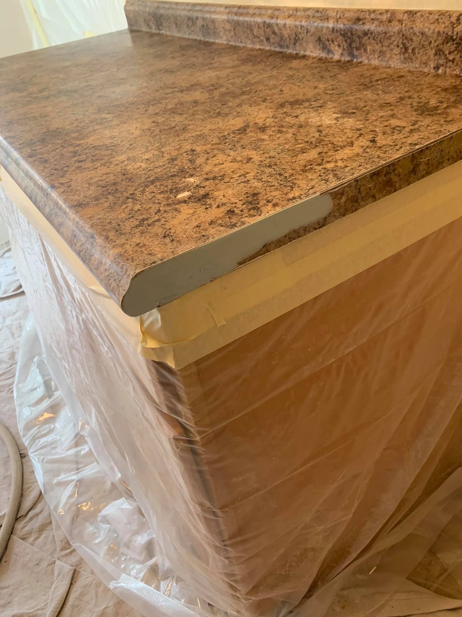 A kitchen counter is covered in plastic wrap and is being painted