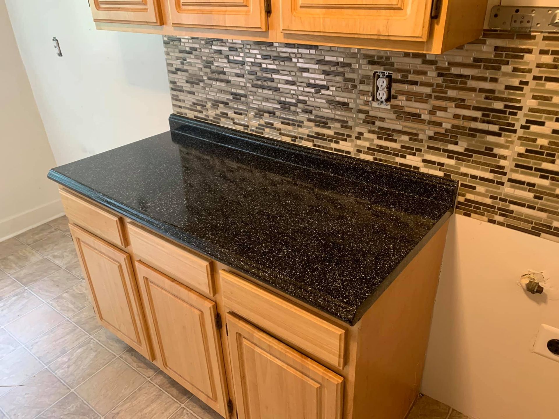 A kitchen counter with a black granite counter top and wooden cabinets