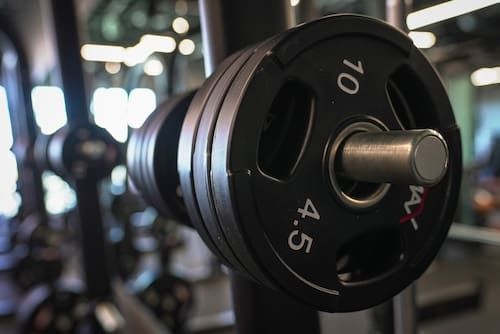 Close-up of a black 45-pound dumbbell on a gym rack, with blurred workout equipment in the background