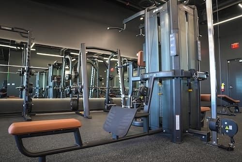 Modern gym with cable machines, mirrors, and an orange-padded bench