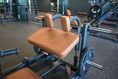 Leg press machine with tan pads in a gym, shown from the side.