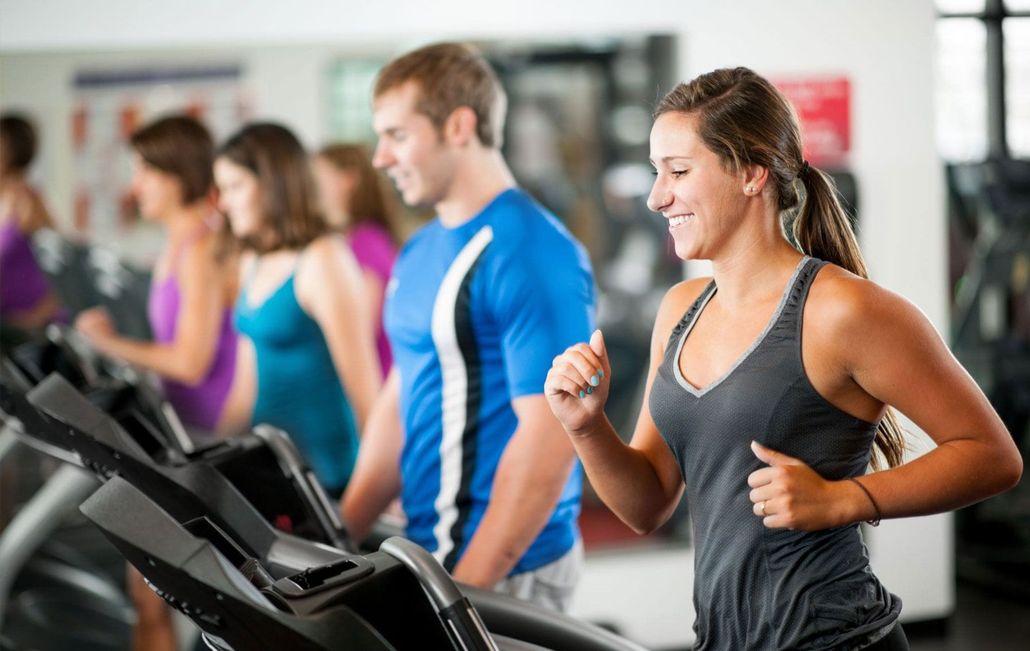 People jogging on treadmills in a gym, with one woman smiling in the foreground.