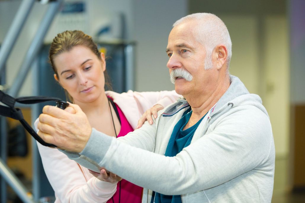 Older man exercising with a trainer in a gym, using a cable machine